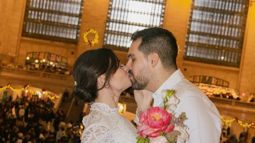 A couple is kissing in a warmly lit indoor setting with wooden interior and string lights.