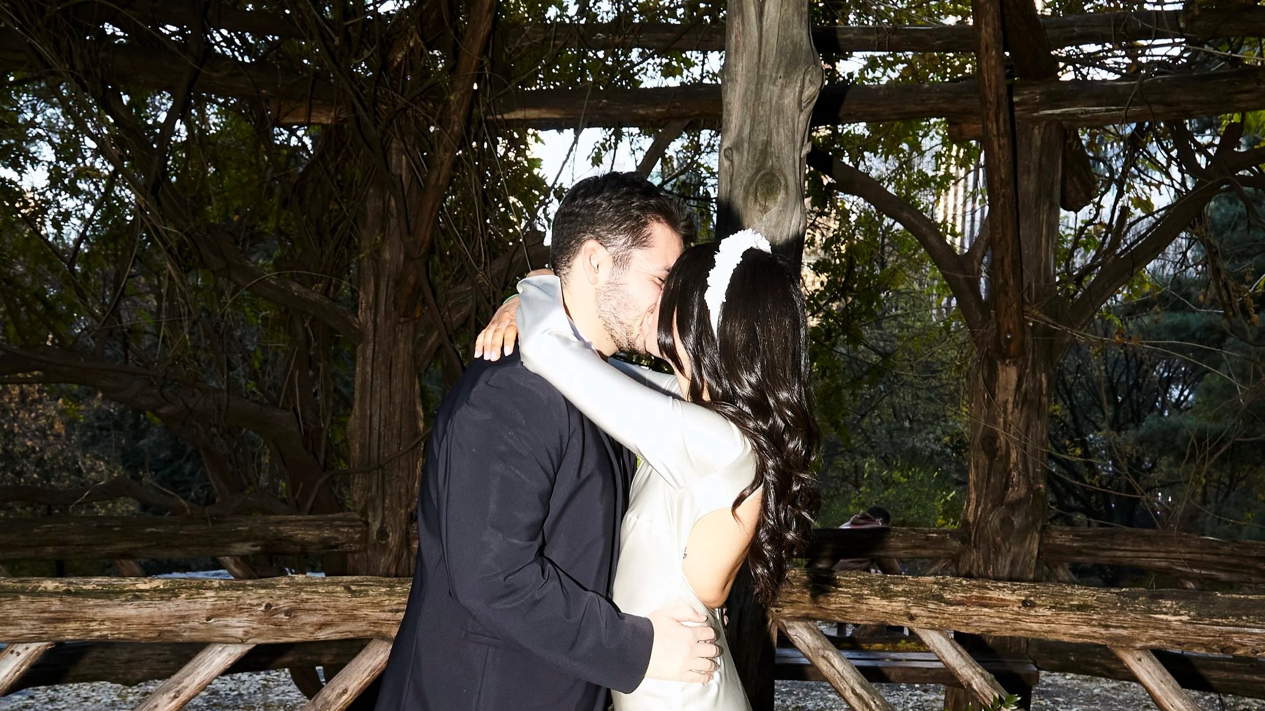 Sharifa and Jafar kissing during their Cop Cot ceremony in Central Park, surrounded by autumn foliage.
