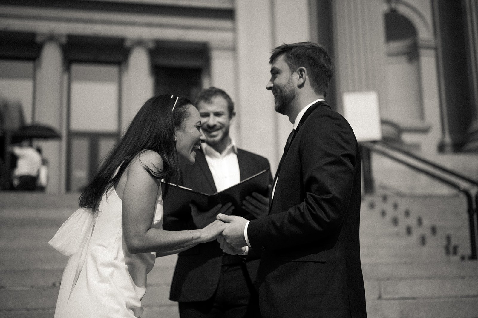 Bride and groom holding hands and laughing in front of their officiant on the Met Museum steps at their Cakewalk elopement ceremony.
