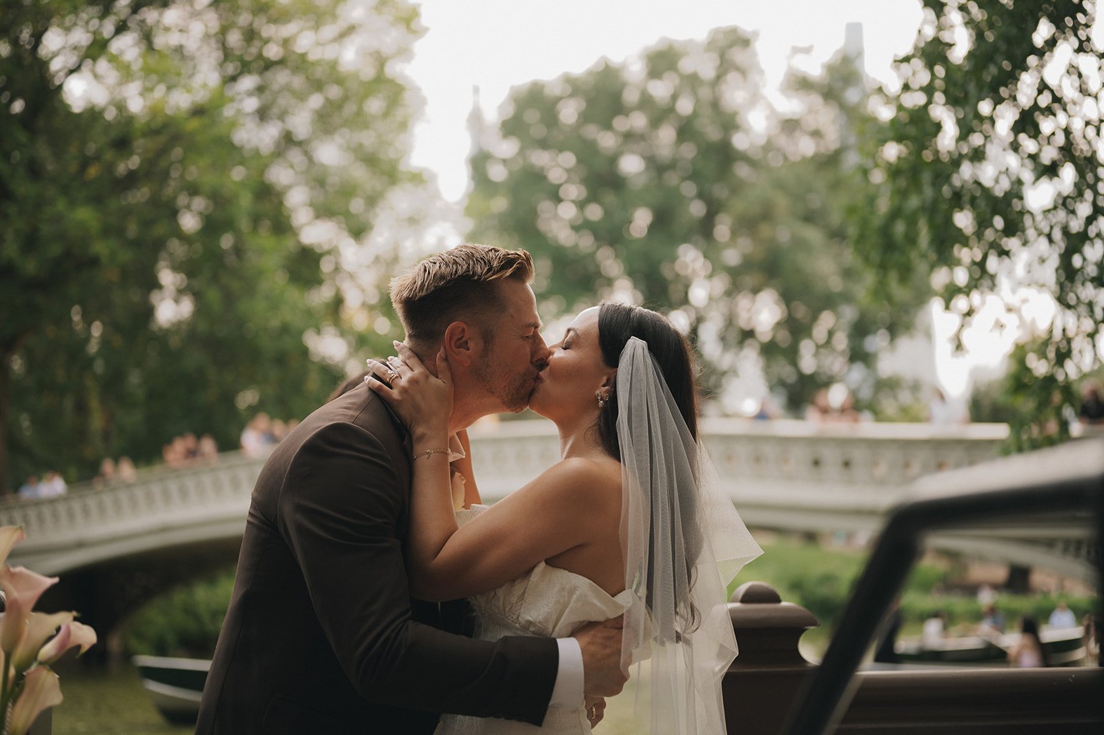 Bride and groom kissing in front of Bow Bridge after Central Park elopement ceremony near the water.