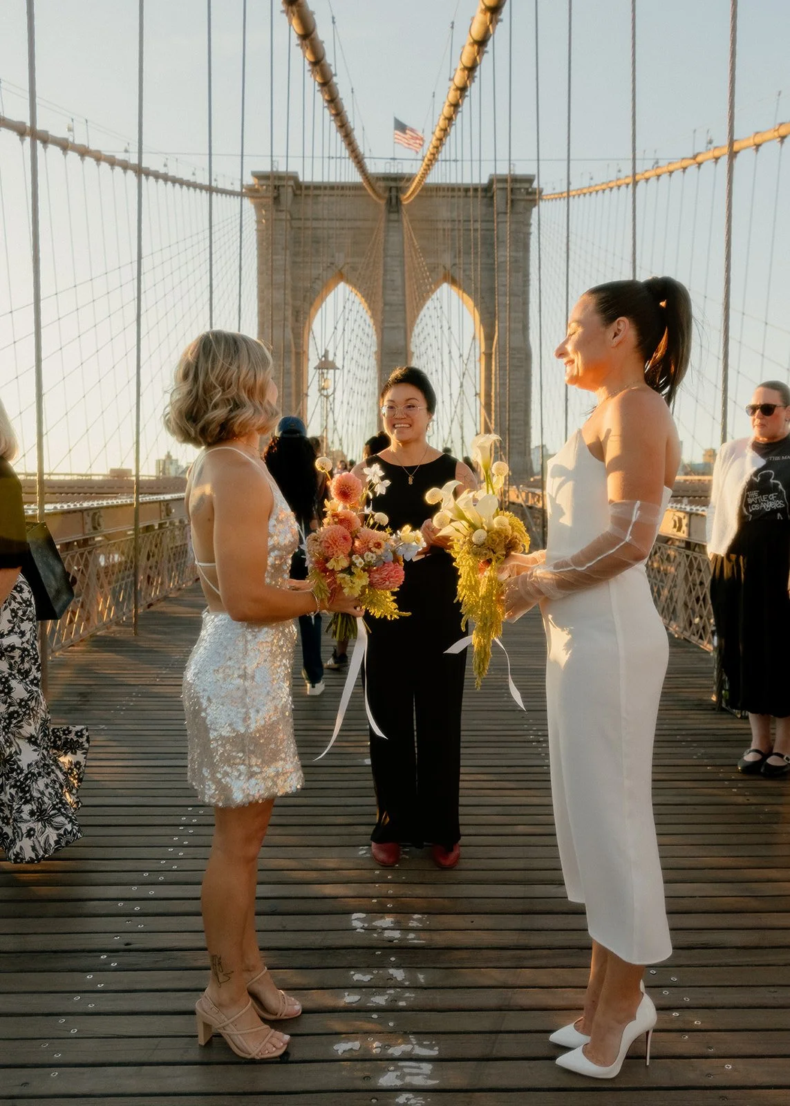 Two brides exchange vows during a sunrise elopement on the Brooklyn Bridge in New York City, officiated by a NYC-registered celebrant.