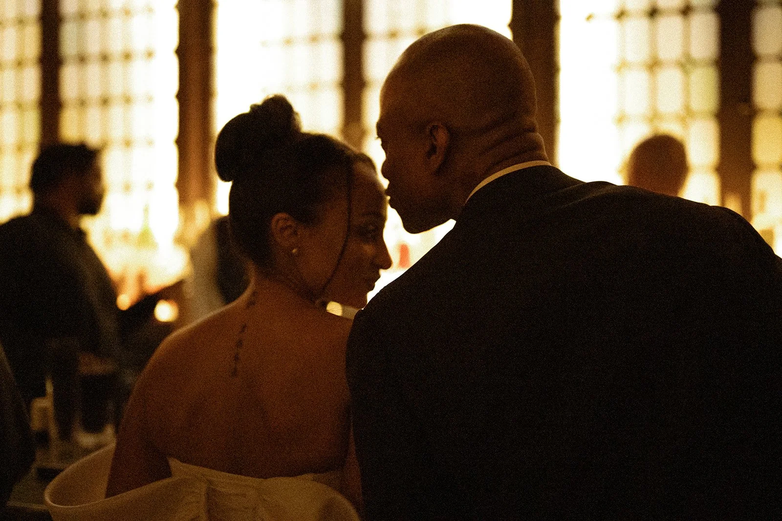 Bride and groom leaning towards each other at a bar, with glowing gold windows behind them.