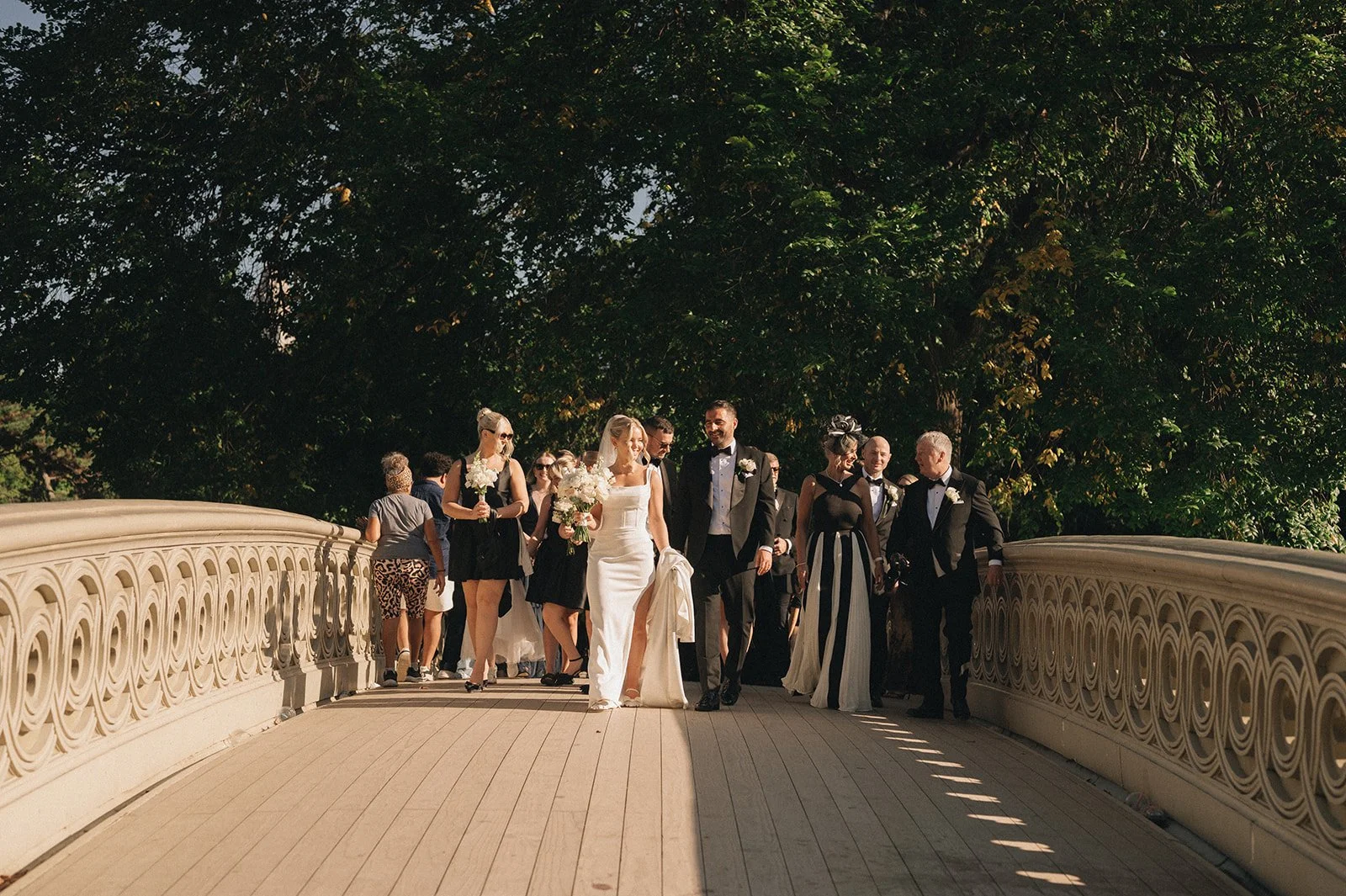 Bride, groom and guests walking across Bow Bridge in Central Park after their Cakewalk wedding ceremony.