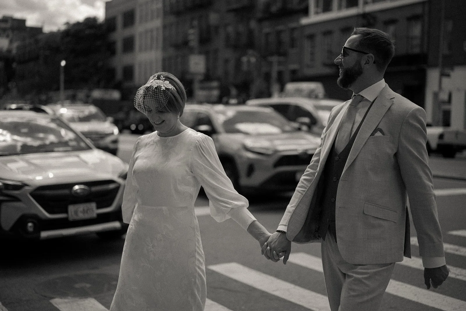 Bride and groom crossing the crosswalk on a SoHo street in front of many cars and buildings after their Cakewalk elopement. 