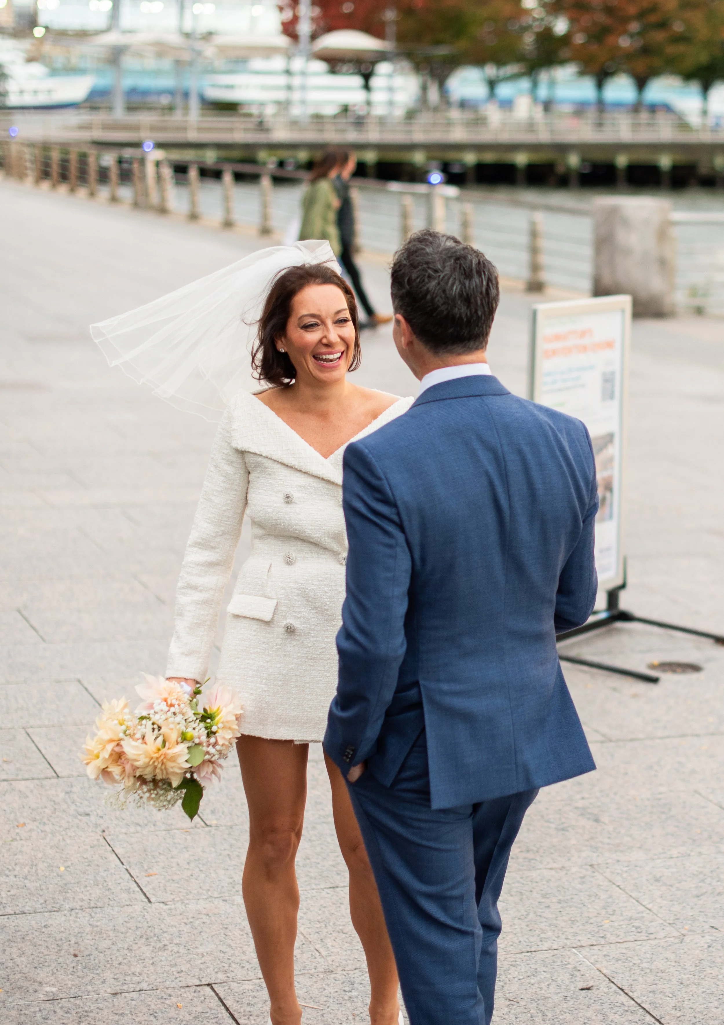 Bride and groom arriving at Hudson River Park, bouquet in hands, water and bridges in the background.