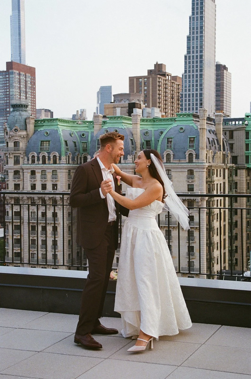 A newlywed couple dancing on a rooftop with New York City skyscrapers in the background.
