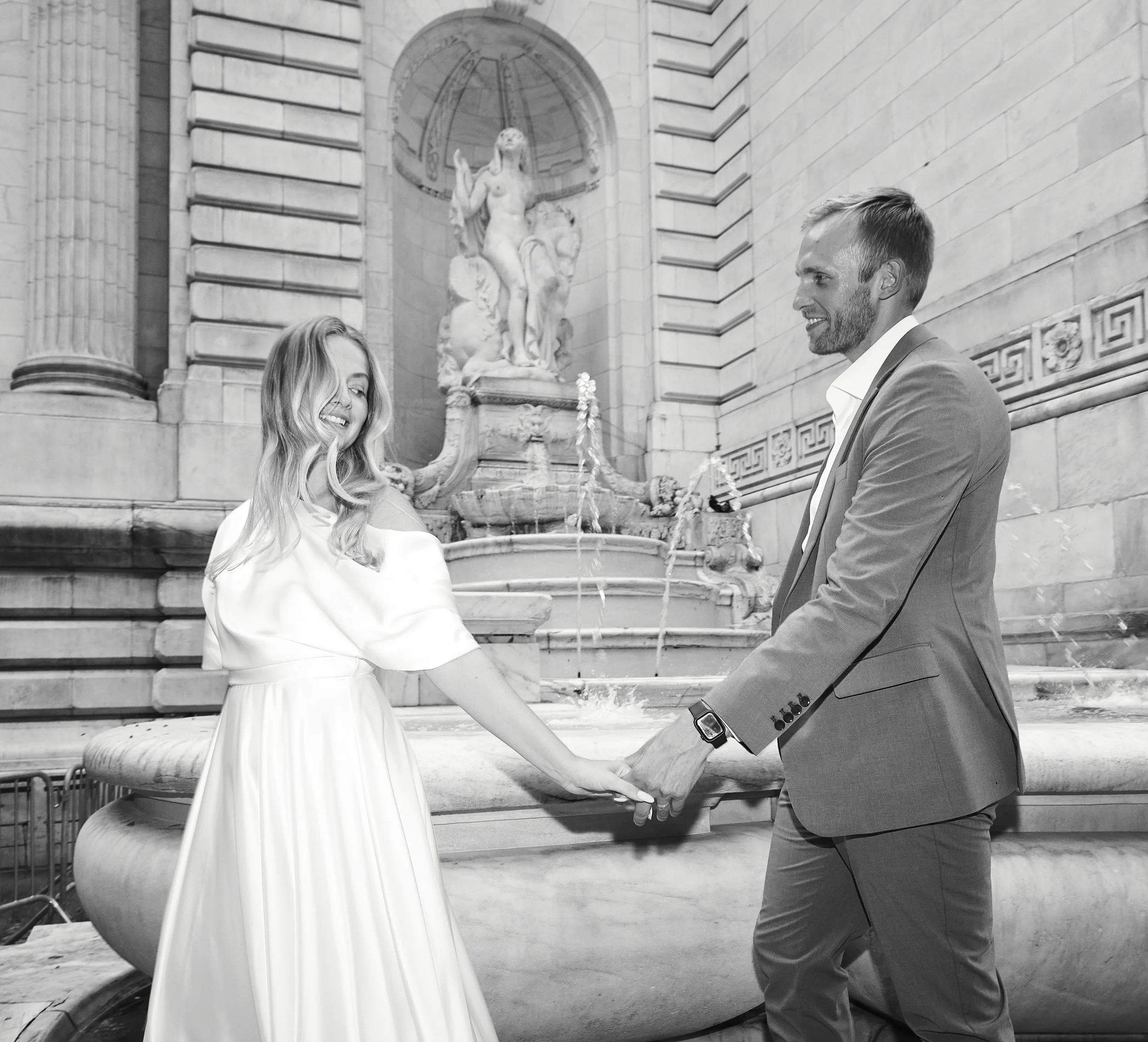 Bride and groom holding hands and walking in front of the fount at Bryant Park after their Cakewalk elopement.