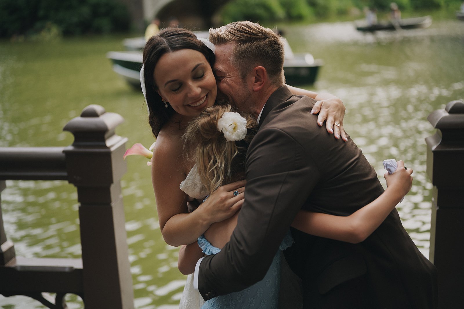 Bride, groom, and daughter hugging each other at their Bow Bridge, Central Park elopement ceremony by Cakewalk.