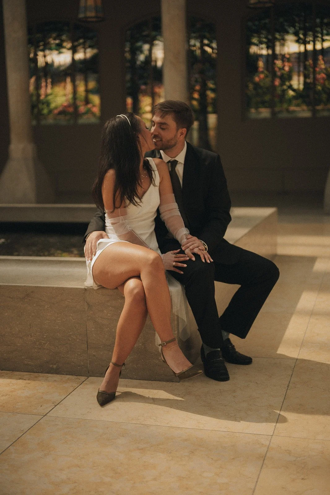 Couple sharing a kiss inside The Met’s American Wing surrounded by stained glass and soft natural light.