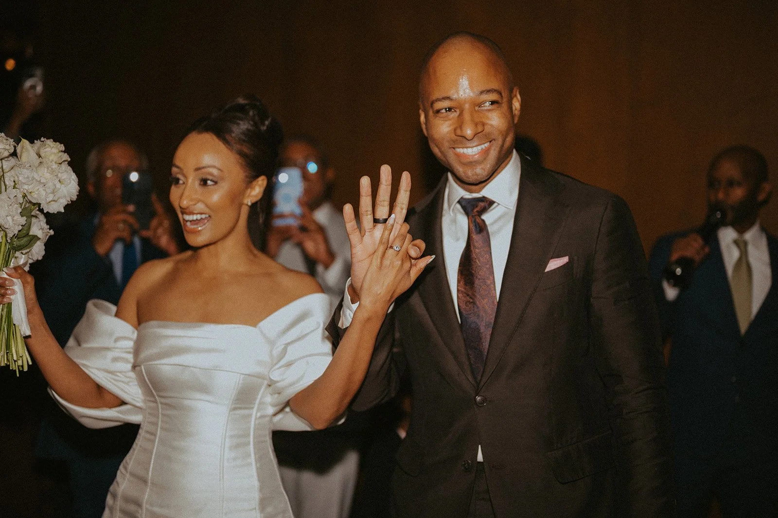 Bride and groom smiling and waving while entering a reception after their Cakewalk micro wedding.