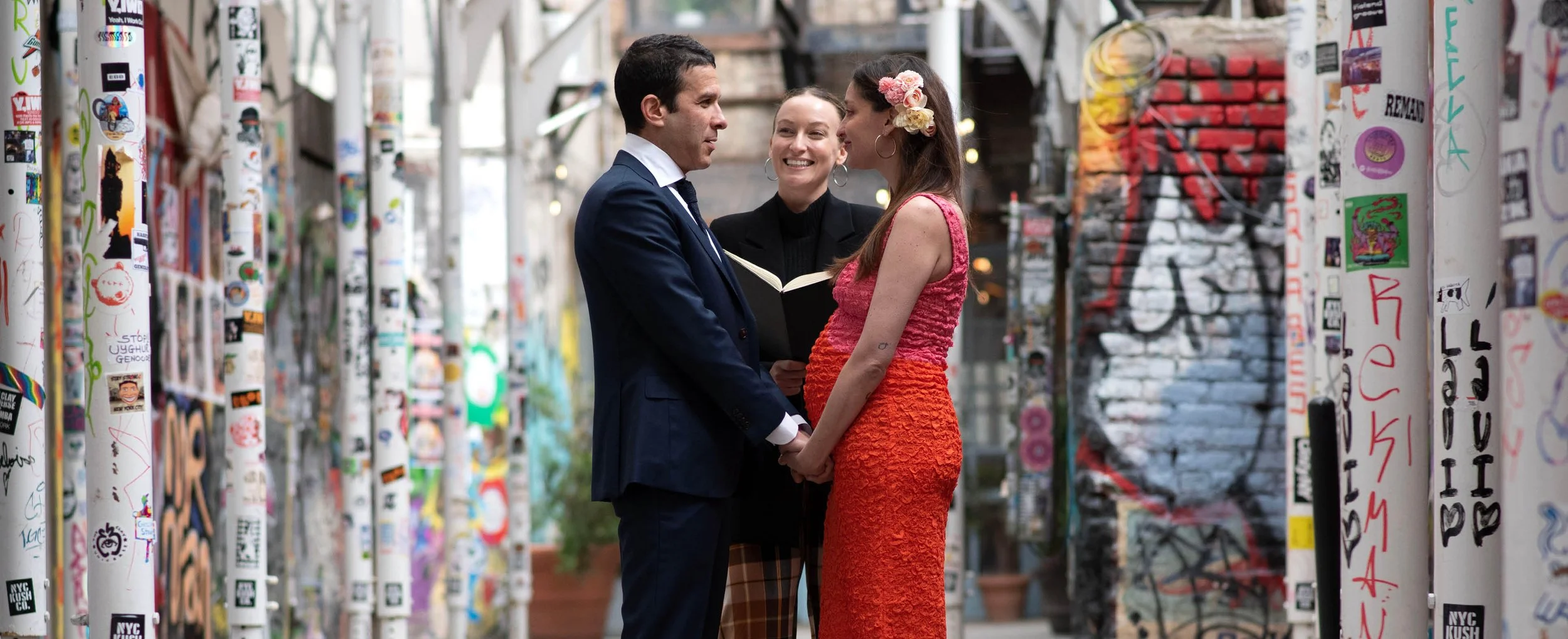 Eloping couple hold hands and say their vows with wedding officiant during their tiny ceremony in Freeman Alley, Manhattan with the help of NYC wedding planner before their NYC wedding reception.