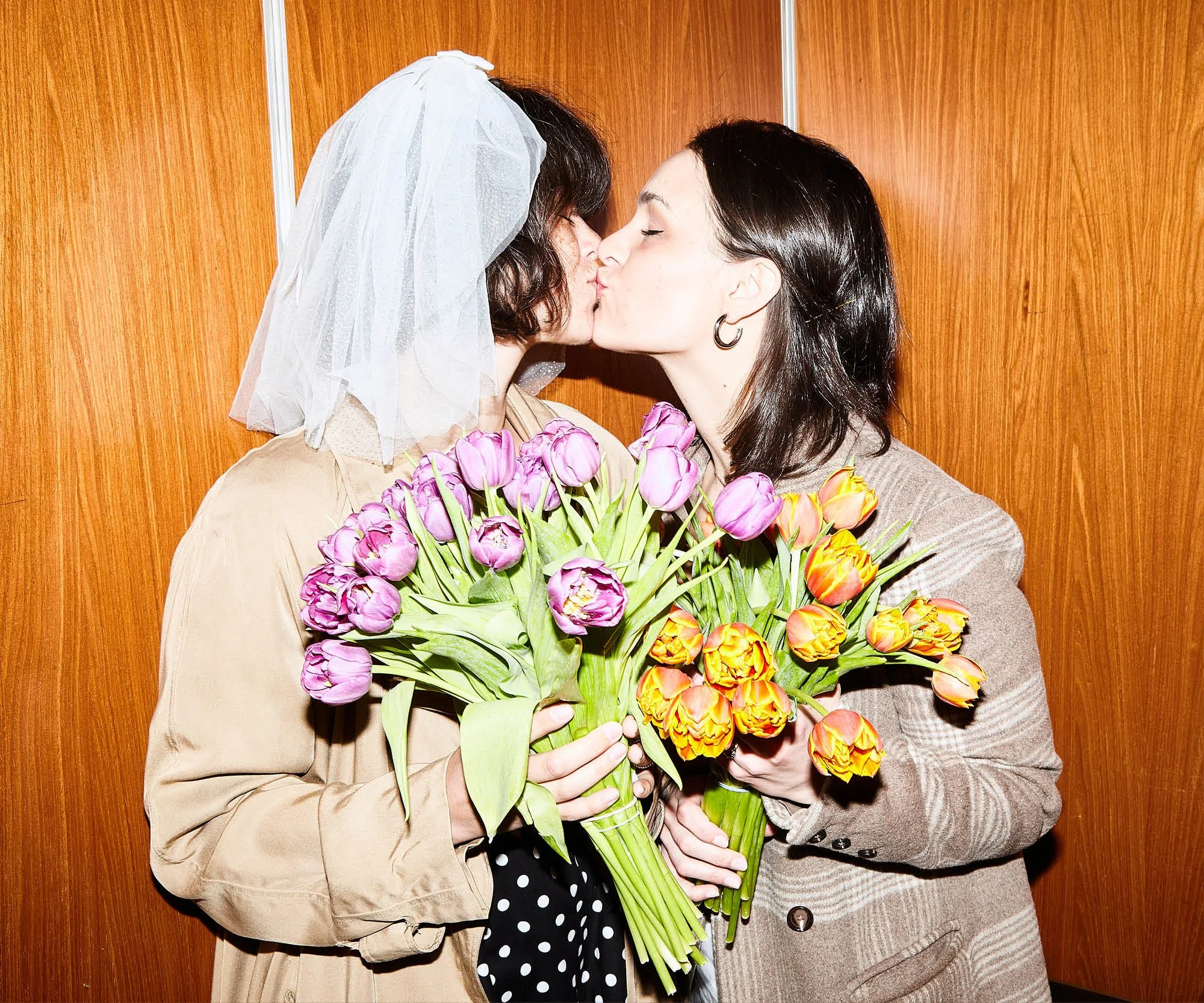LGBT eloping couple kiss for wedding photos in the elevator of their Fort Greene Park apartment before their elopement ceremony in Brooklyn, New York after they plan a small wedding.