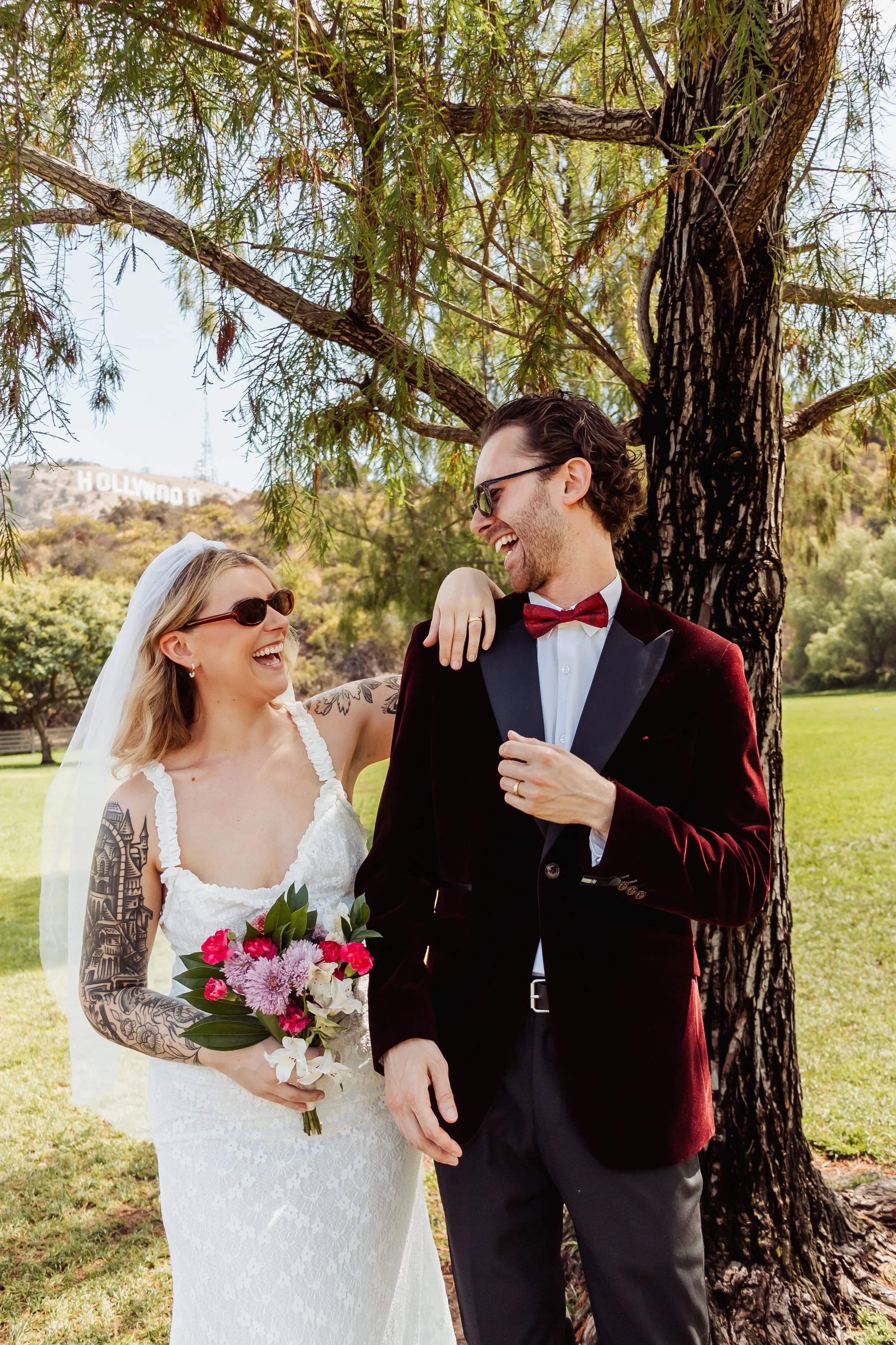 Couple laughing at Lake Hollywood Park with  the Hollywood sign in view under a tree.
