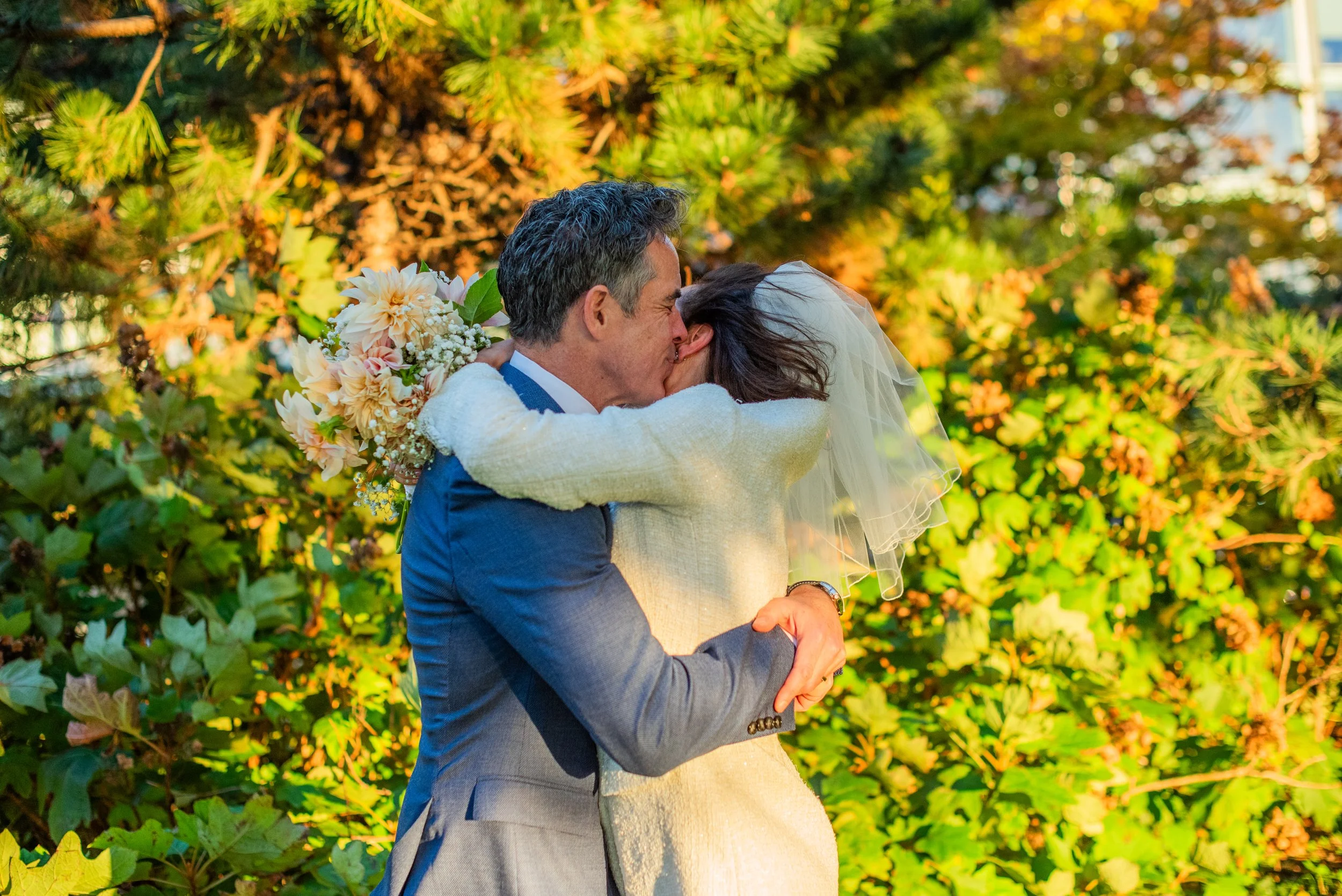 Bride and groom embracing around the trees at Hudson River Park, bouquet in hands, celebrating their Cakewalk elopement ceremony.