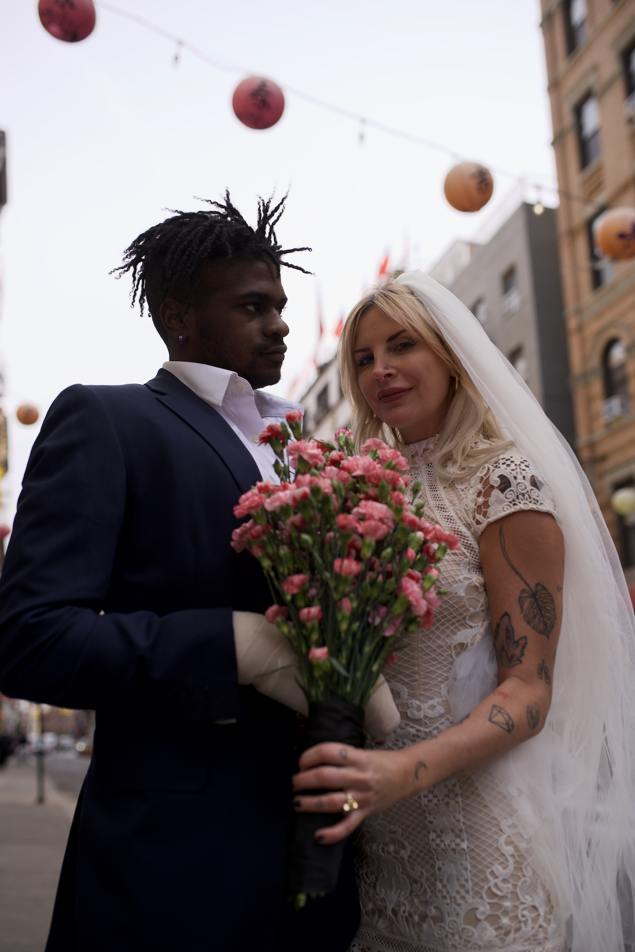 Bride and groom posing under lanterns hanging in Chinatown, holding flowers after their Cakewalk elopement.