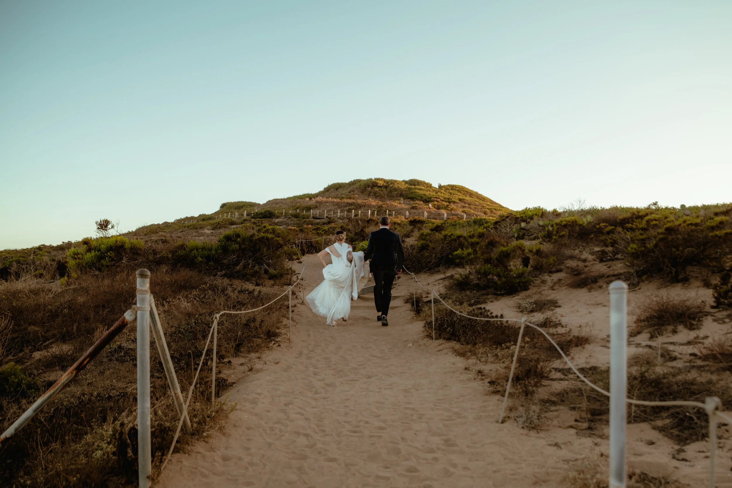 Bride and groom walking toward the hill on Point Dume pathways after their Cakewalk micro wedding.