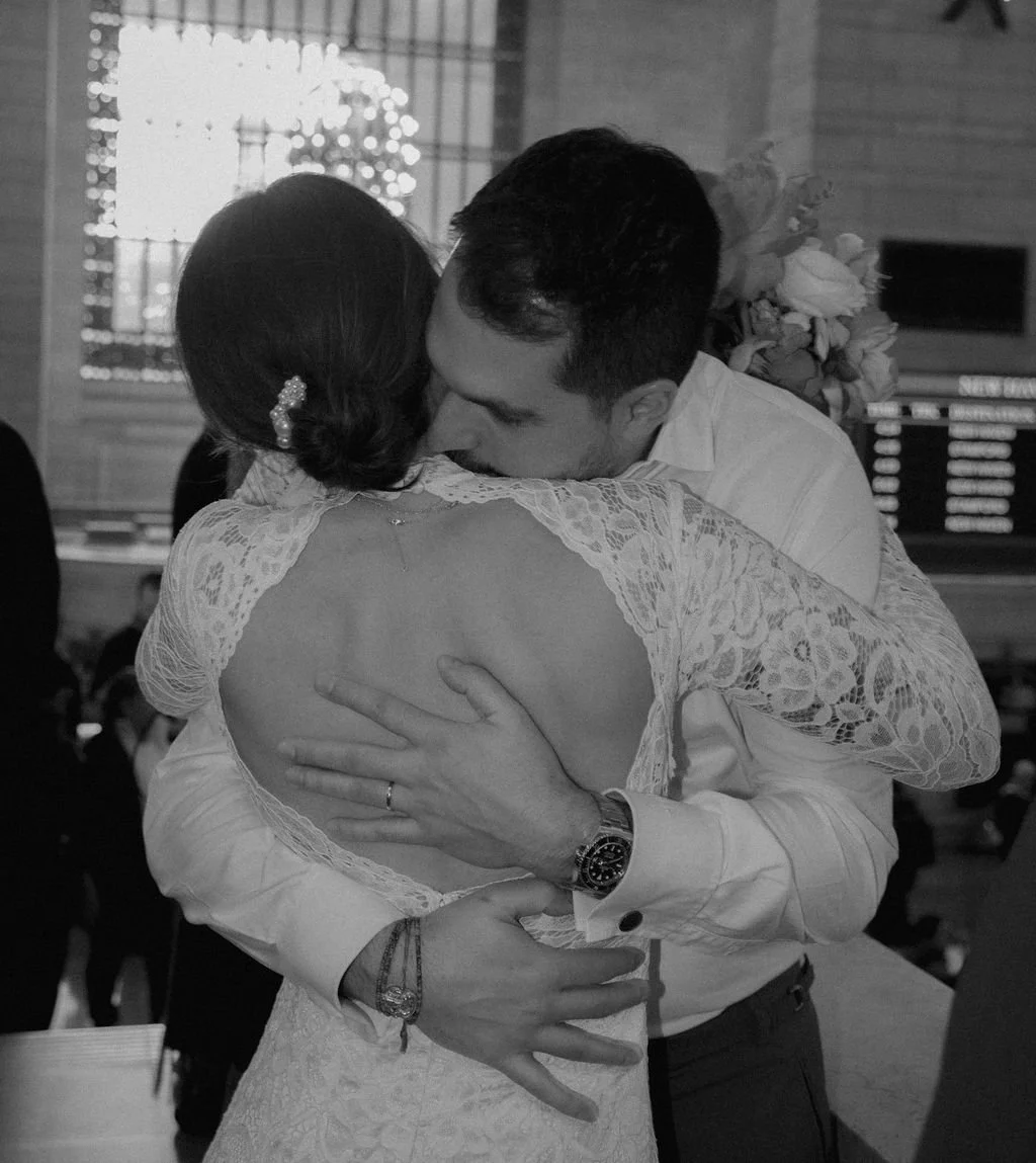 Black and white photo of a married couple hugging in Grand Central Station, NYC.