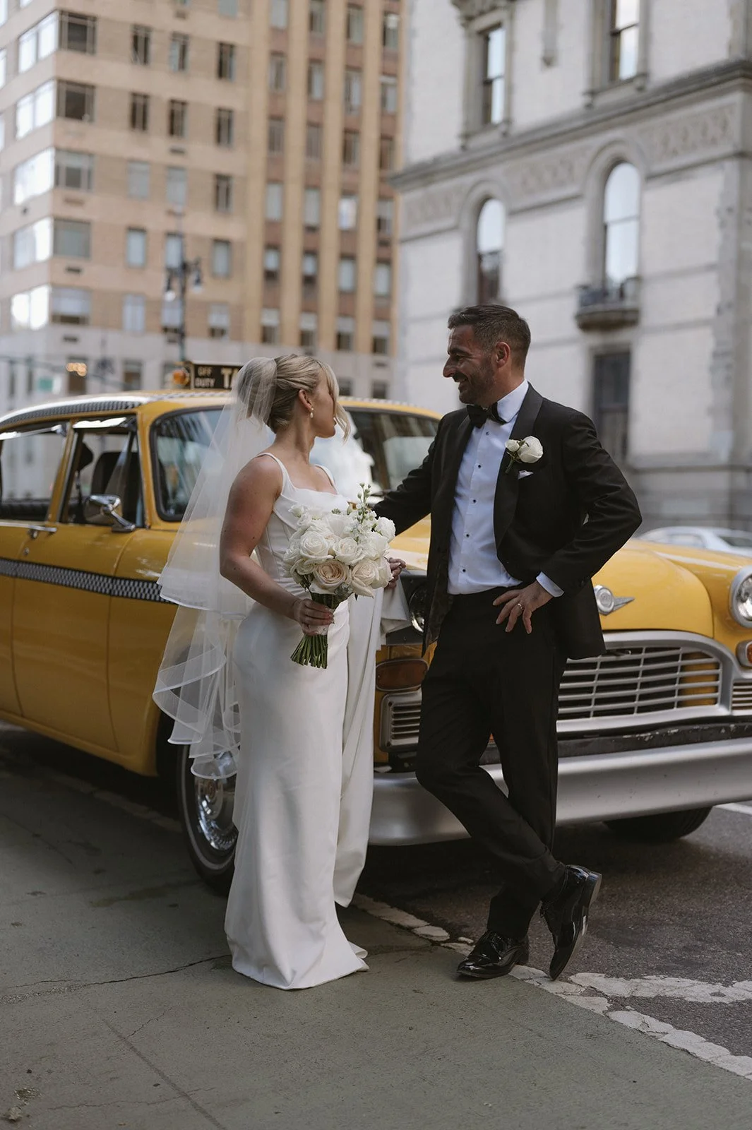 Bride and groom posing in front of a vintage, yellow checkered NYC taxi on the streets of Manhattan.