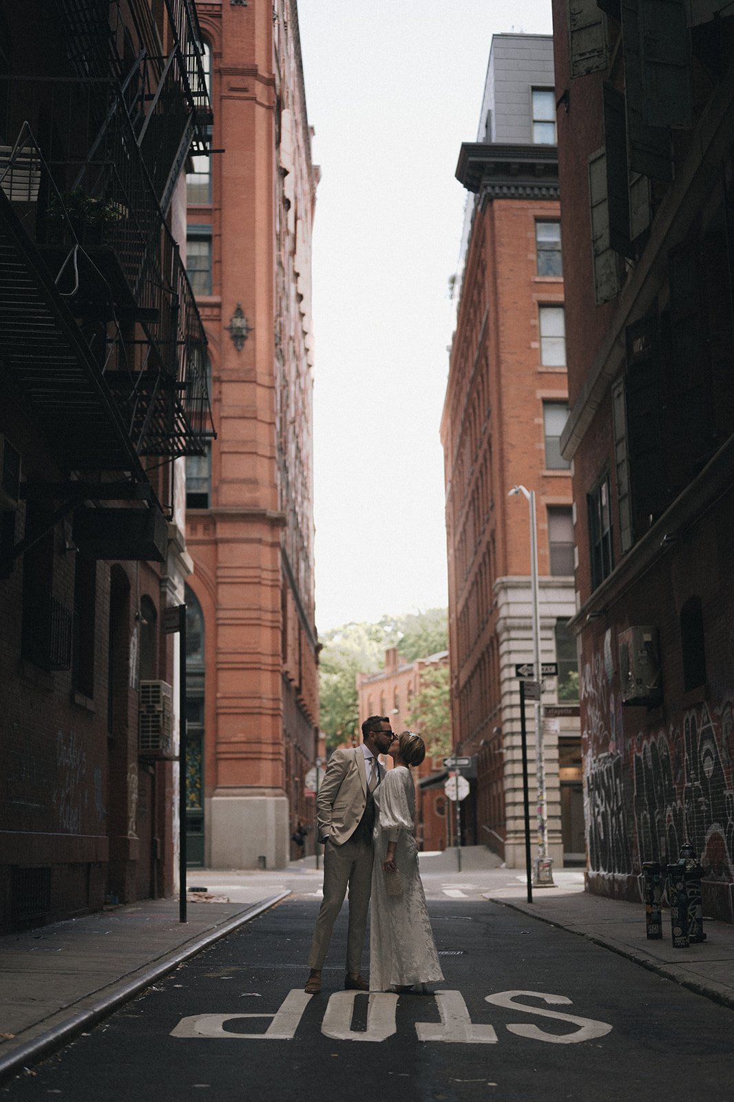 Bride and groom kissing in SoHo streets staring surrounded by tall brick buildings and standing on "STOP" after their Cakewalk elopement. 