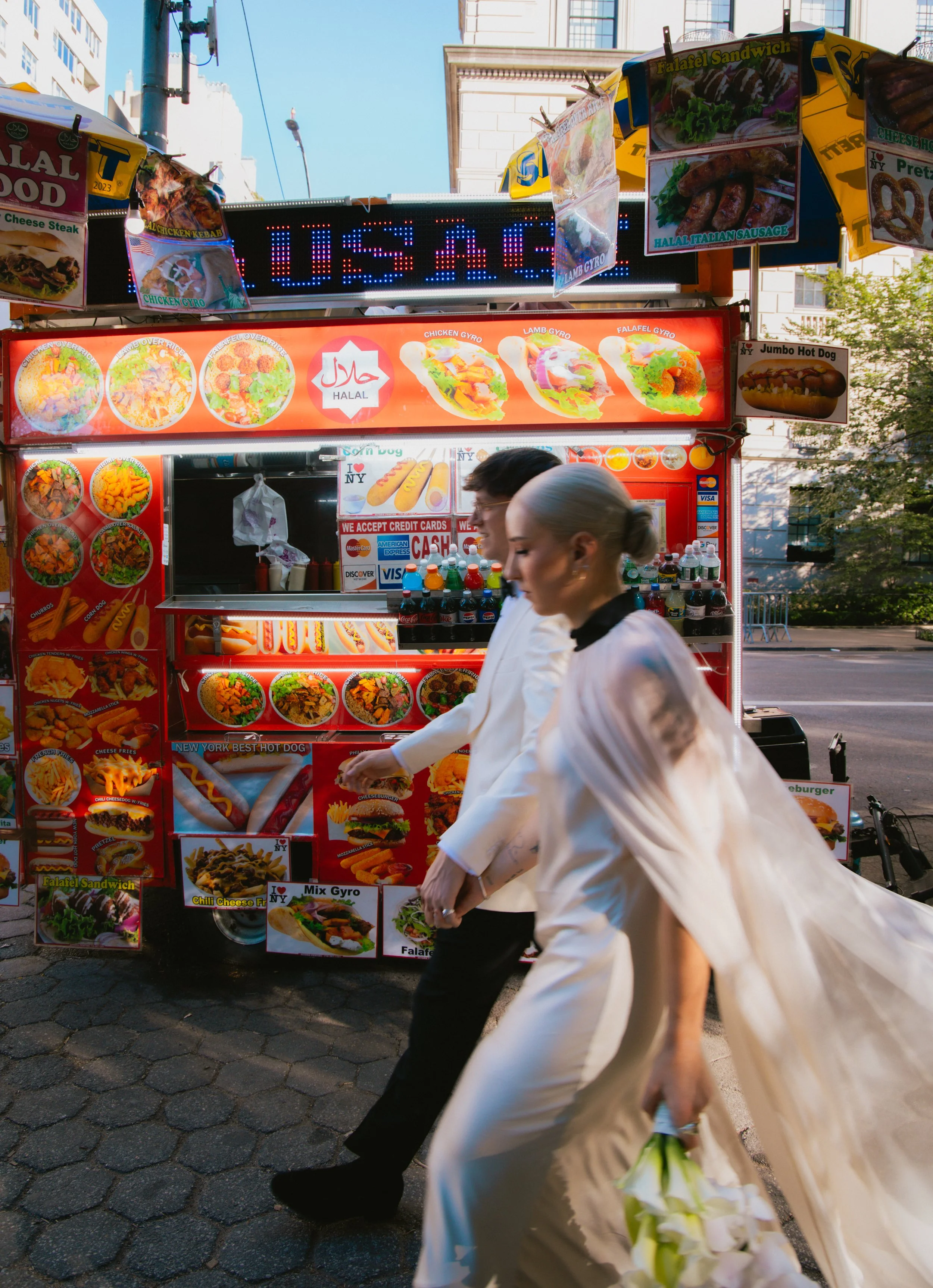 Documentary style photography of a couple walking in front of a hot dog cart in Manhattan on their wedding day.