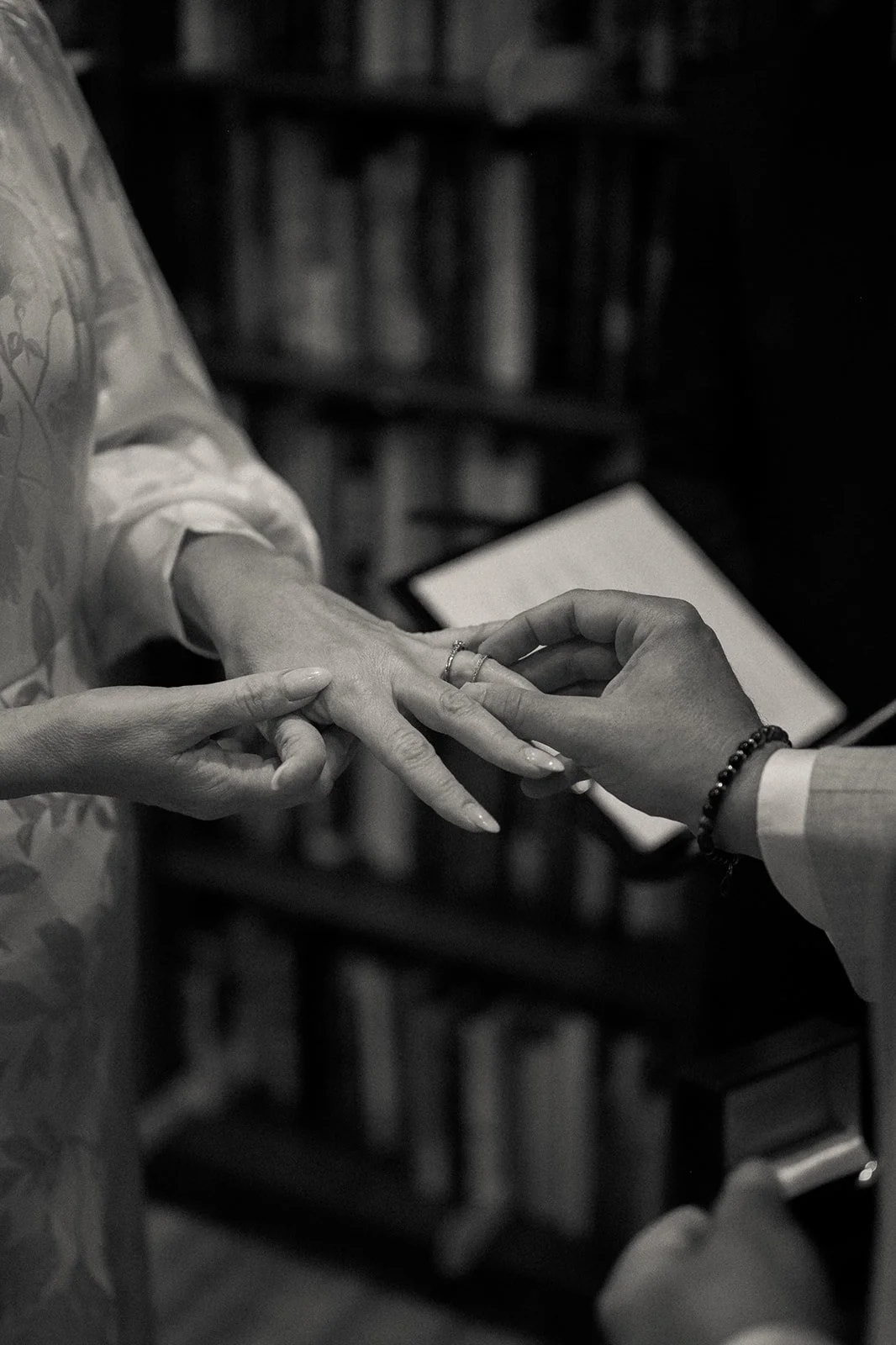 Bride and groom placing rings on each other's fingers with tall bookcases behind them inside Housing Works Bookstore at their Cakewalk elopement ceremony.