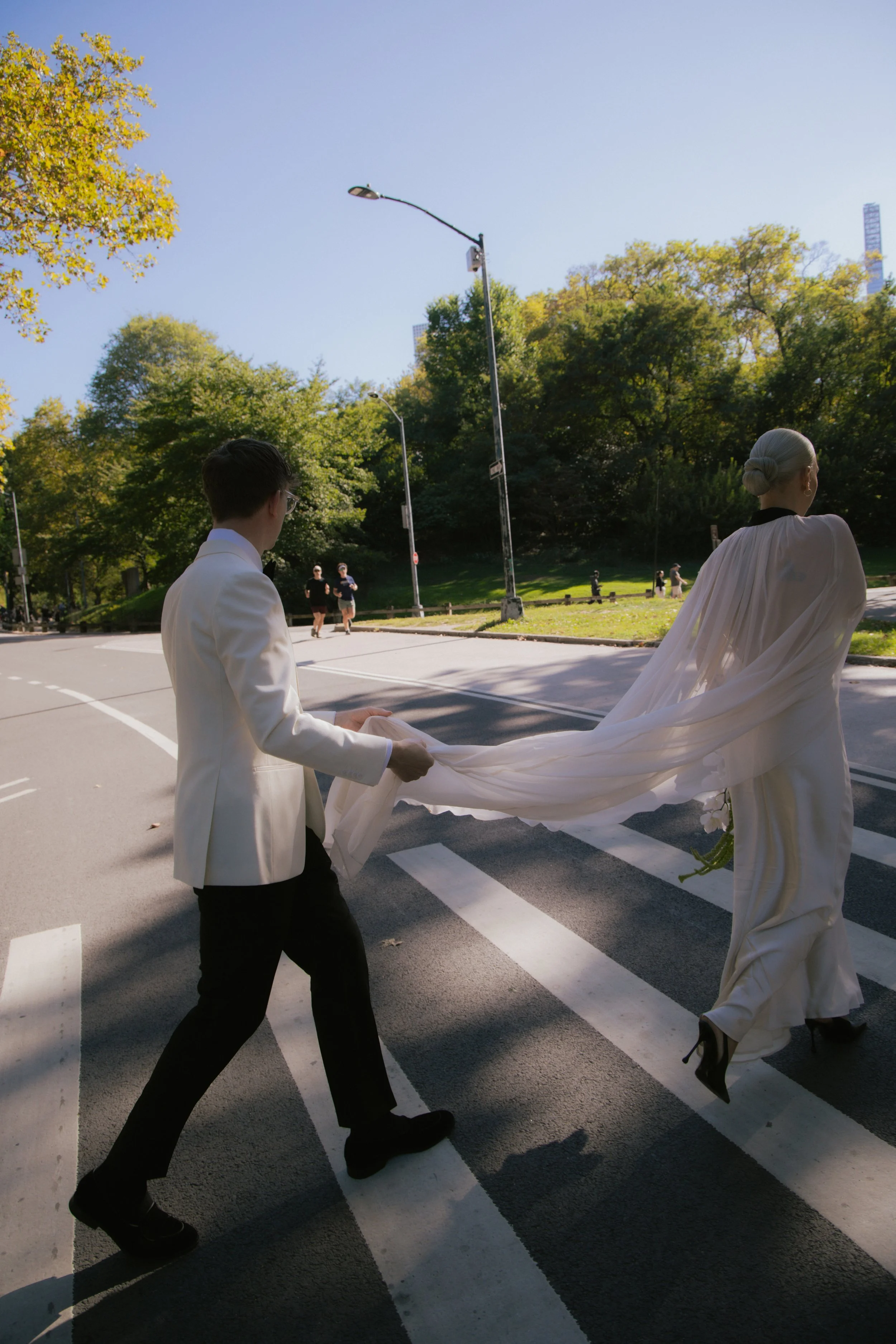 Groom holds bride's shawl while crossing the street at a crosswalk going to Central Park for their Cakewalk elopement.