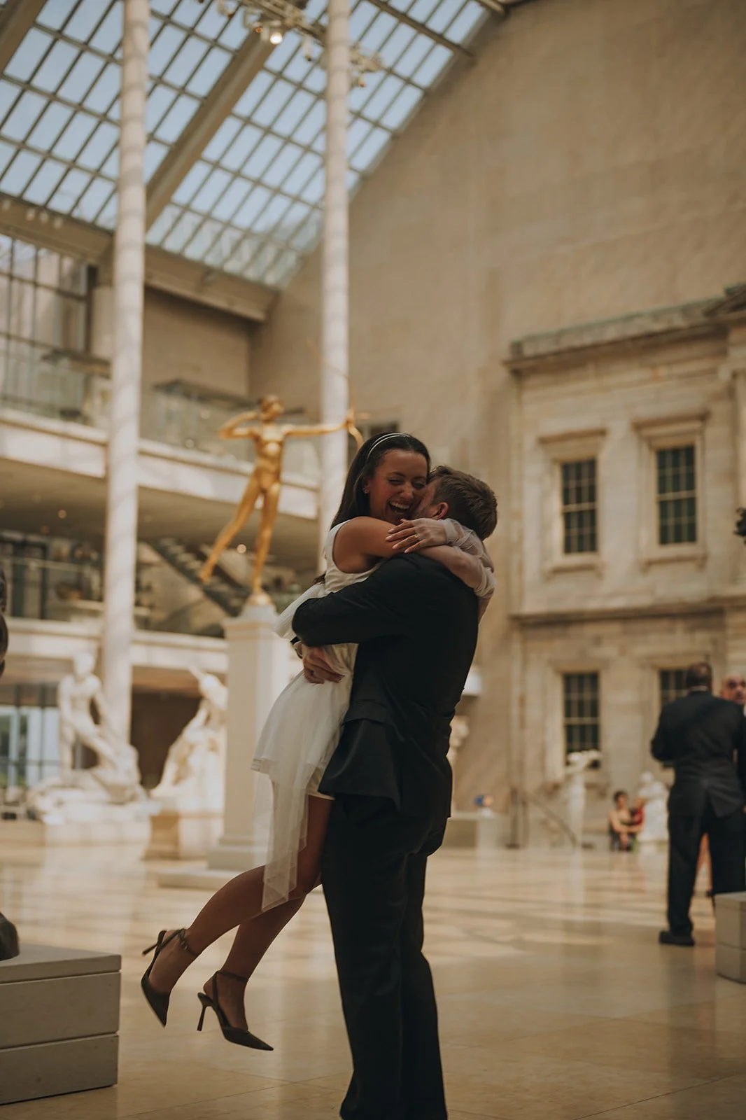 Zach lifting Kayla in a joyful embrace inside the sculpture court at the Metropolitan Museum of Art.