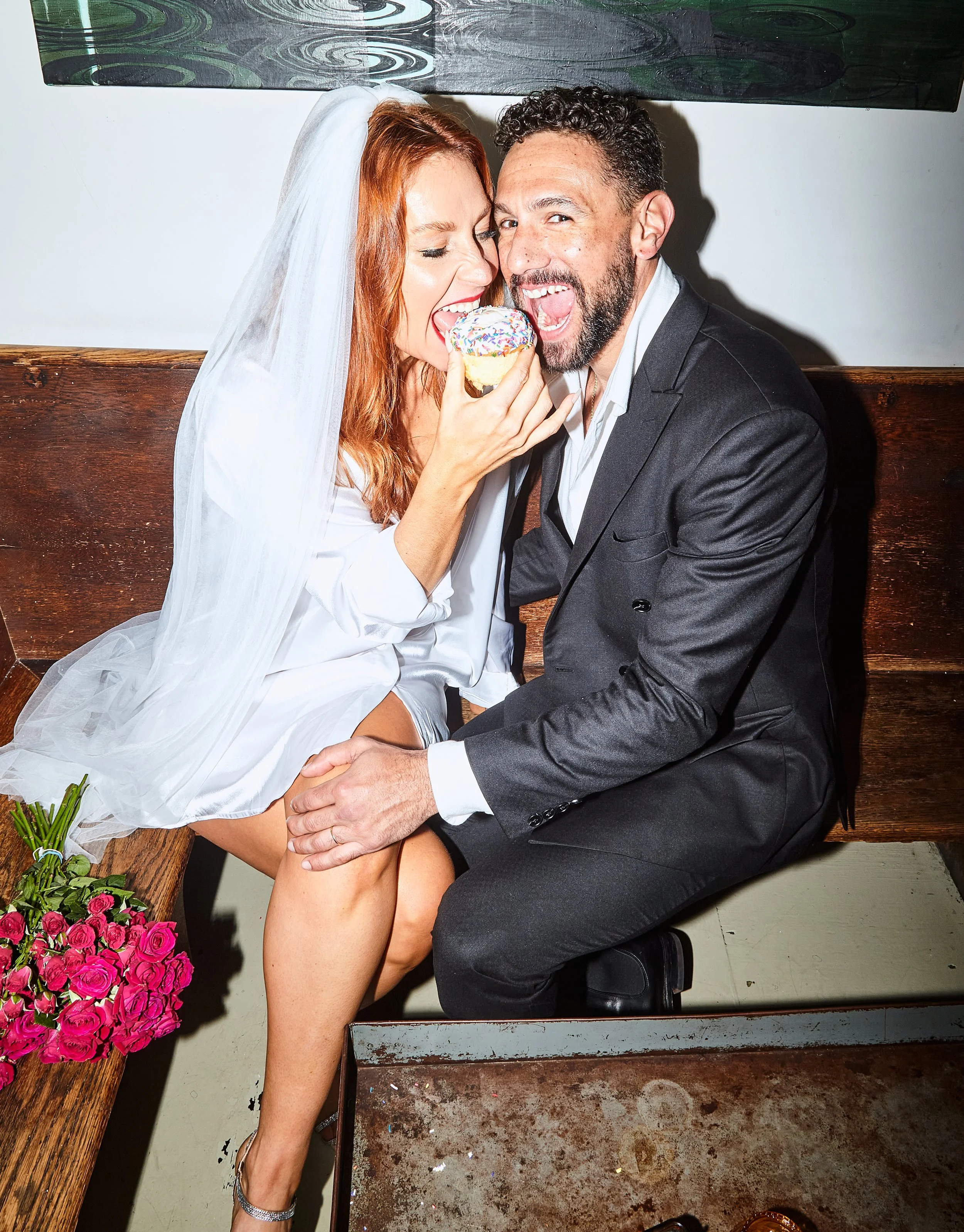 Bride and groom smiling and biting into a donut together after their Cakewalk wedding in Brooklyn.