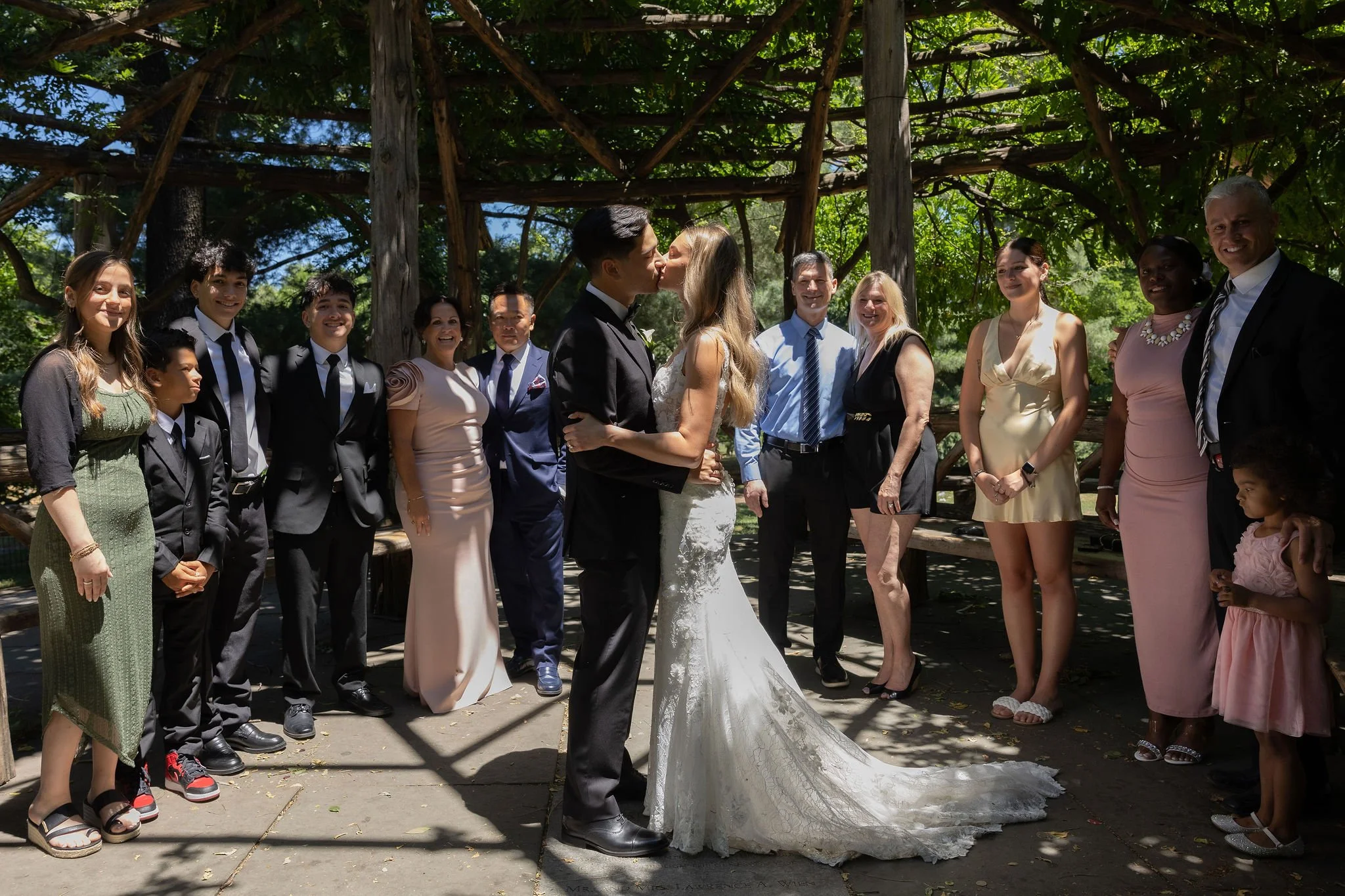 Bride and groom kissing under the gazebo at Cop Cot in Central Park at their Cakewalk micro wedding, with guests onlooking.