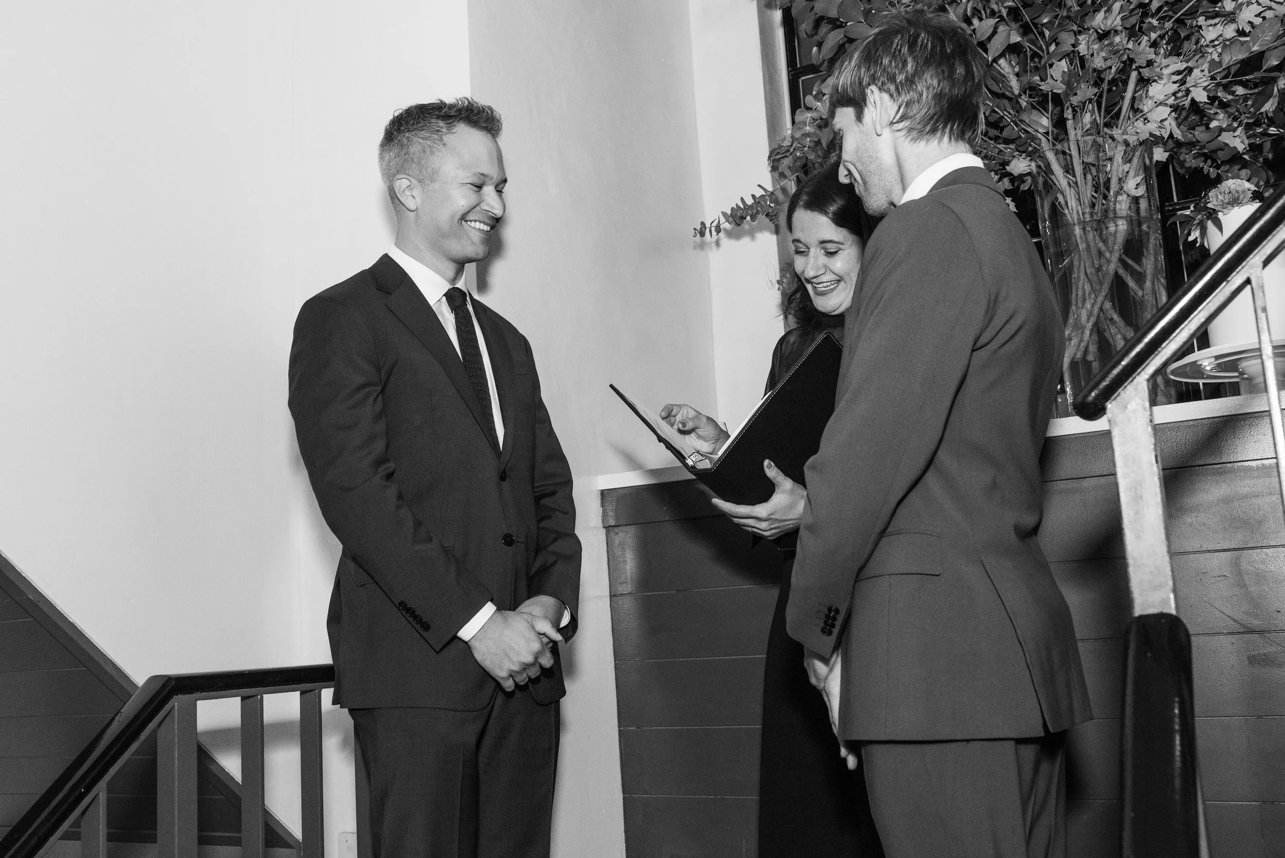 Two men in suits, smiling being married by a female officiant at their Cakewalk micro wedding ceremony. 