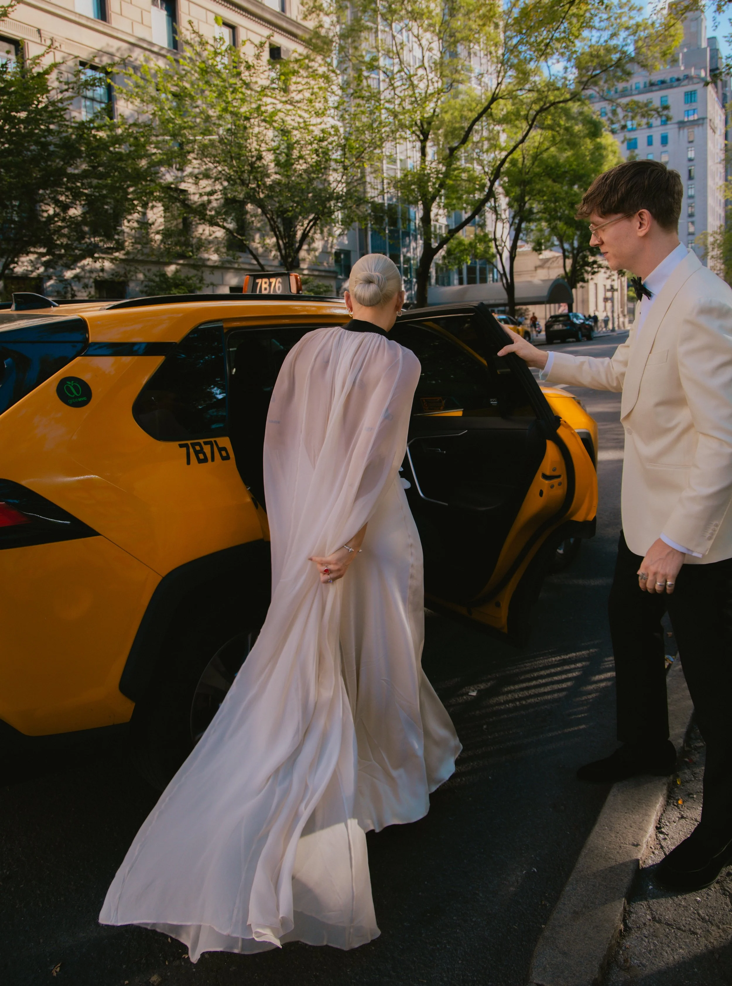Groom holding a yellow cab door as bride enters on the way to explore Manhattan on their wedding day.
