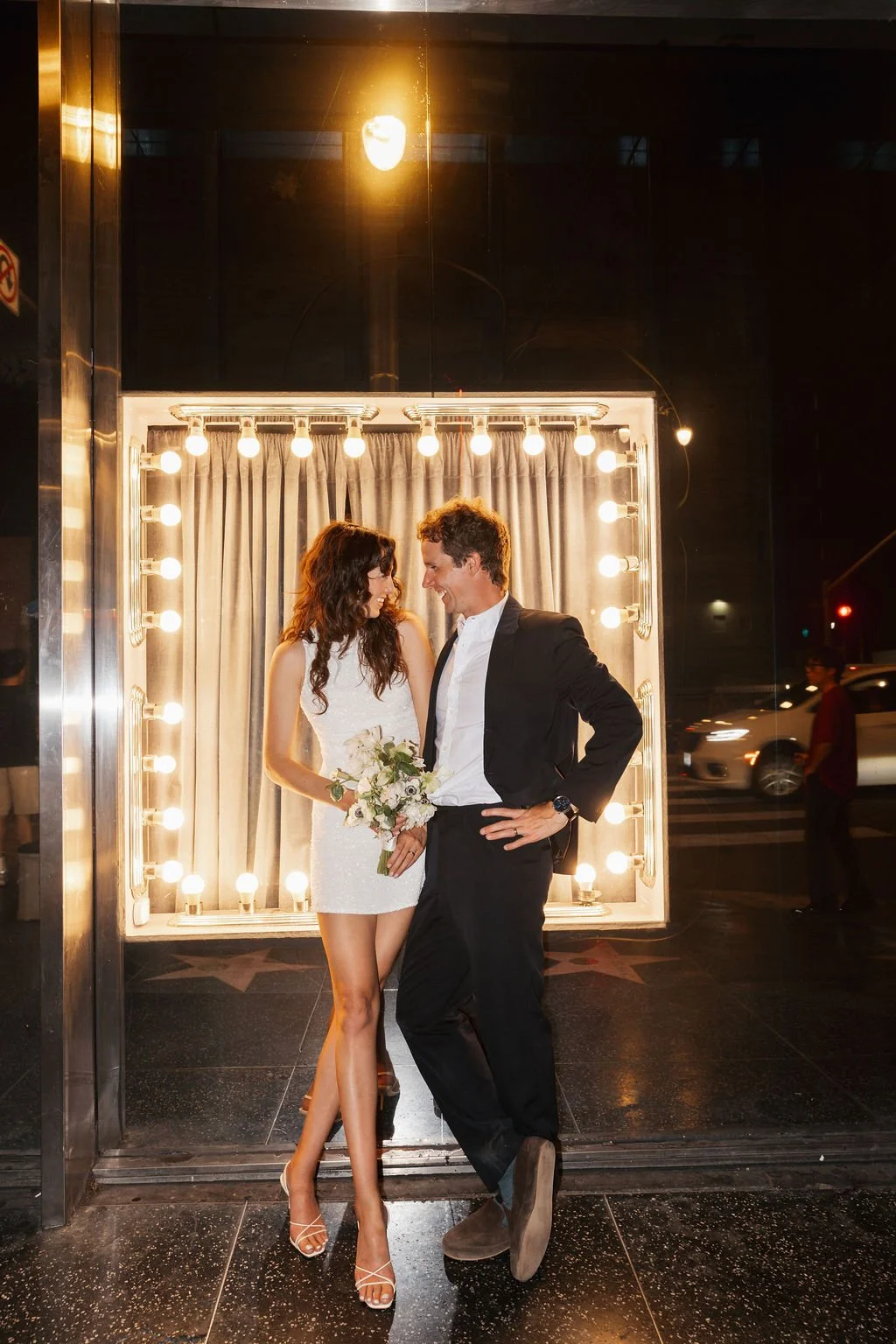 Couple posing in front of lights on Hollywood Blvd at night in wedding attire.