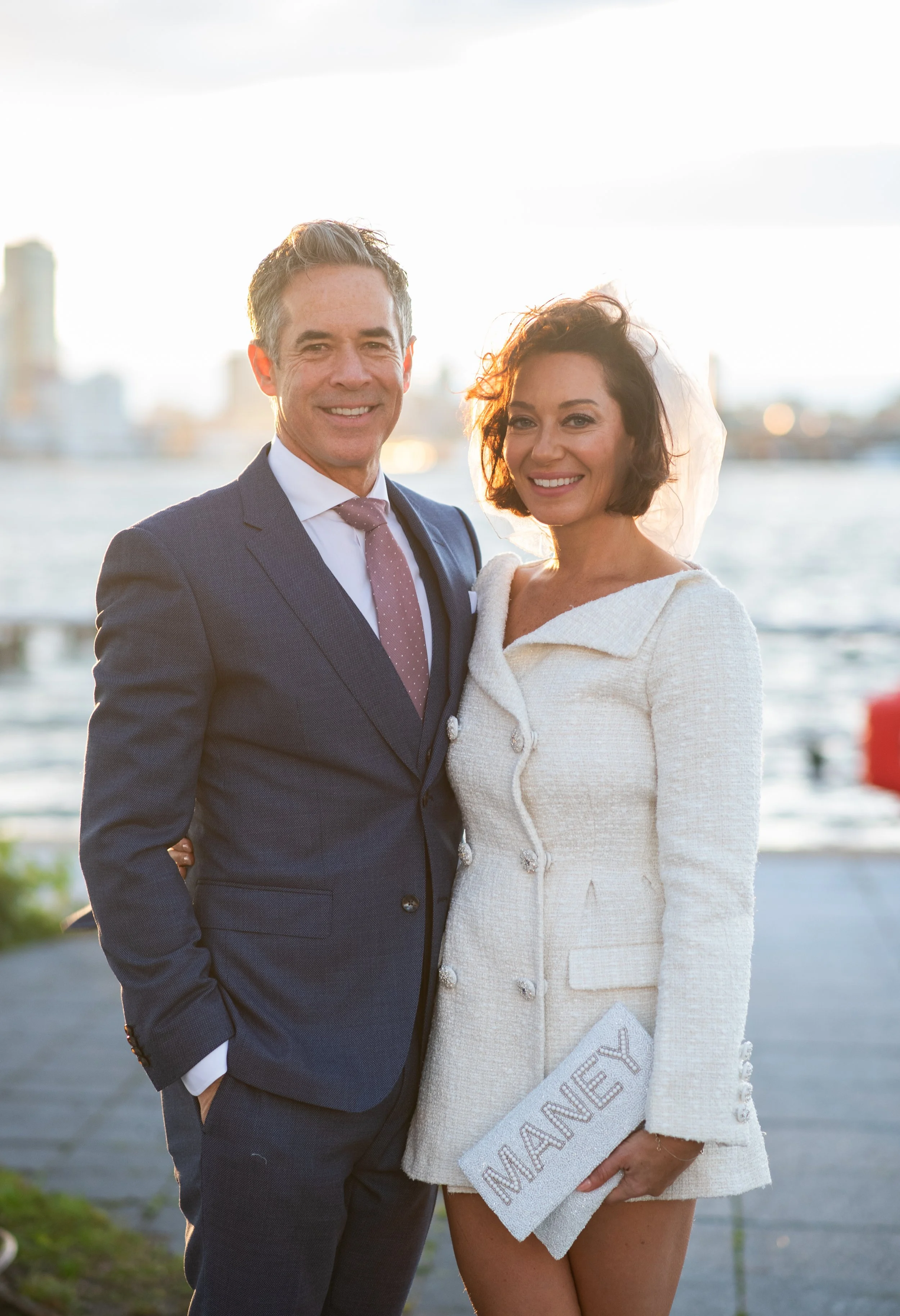 Bride and groom smiling at Hudson River Park with the city and the water behind them after their Cakewalk elopement ceremony.