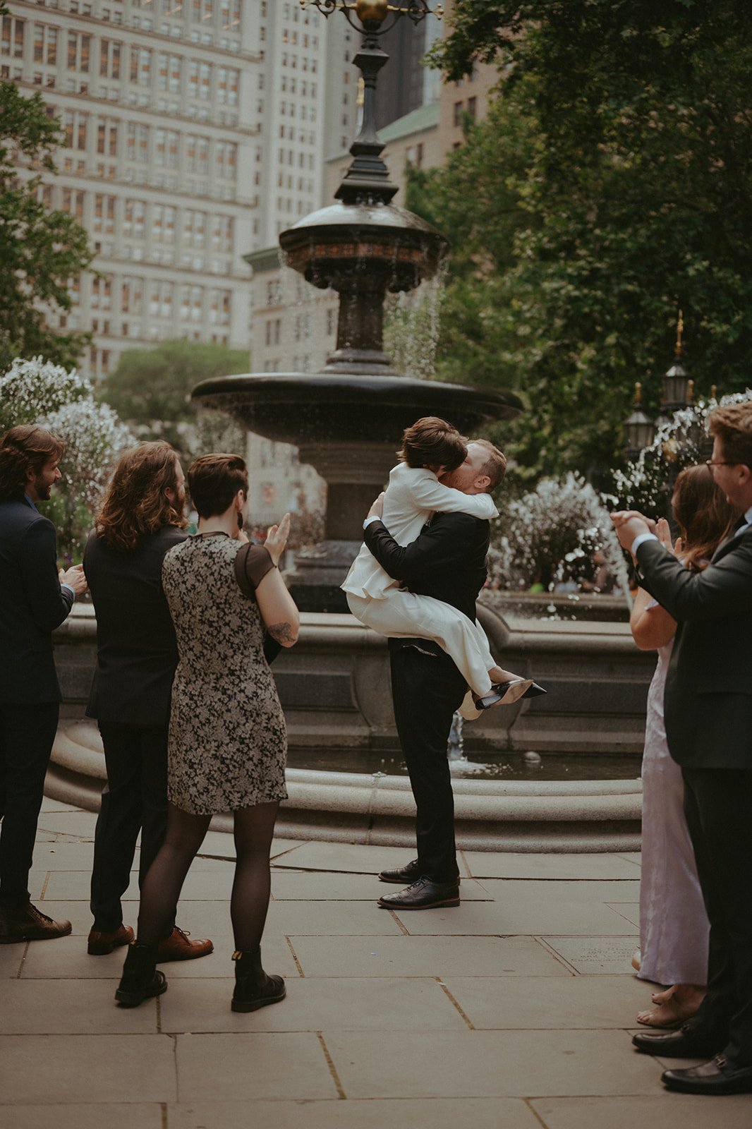 Groom lifting bride by a fountain with guests at their NYC micro wedding ceremony