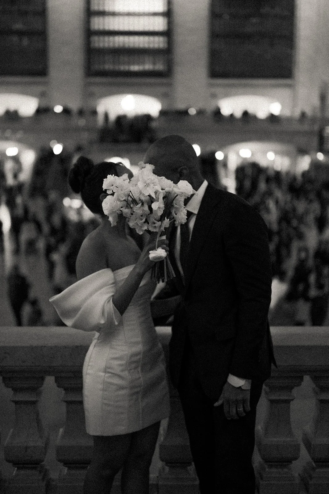Bride and groom covering their faces with a bouquet and kissing on the balcony in Grand Central Station after their Cakewalk micro wedding.