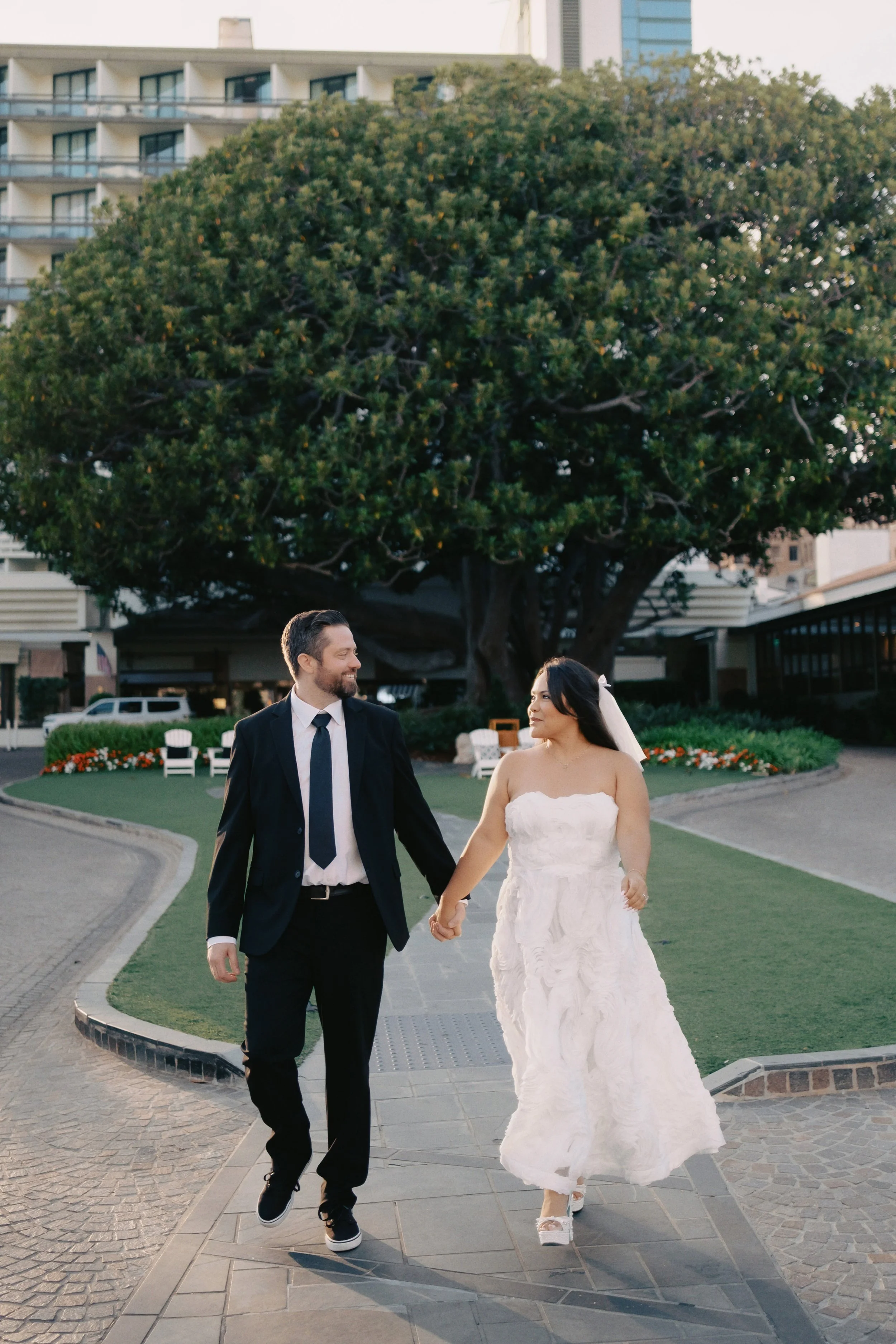 Bride and groom walking in front of a tree at the Fairmont Miramar in Santa Monica before their Cakewalk elopement ceremony.
