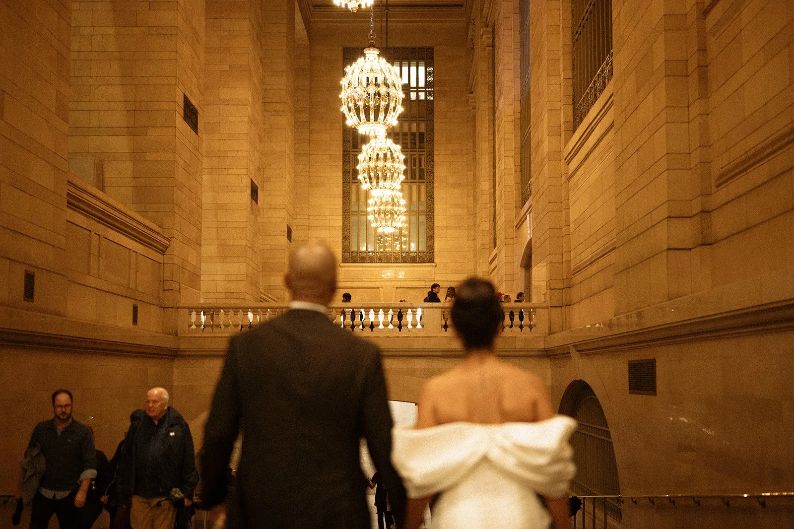 Bride and groom walking into Grand Central Station  with ornate lighting hanging from the ceiling after their Cakewalk micro wedding.