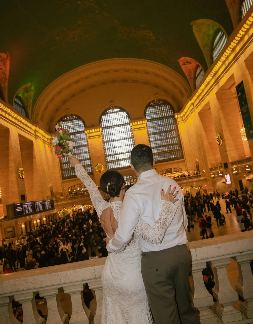 Couple looking out over the balcony after their Cakewalk elopement in Grand Central Station in NYC, holding a bouquet.
