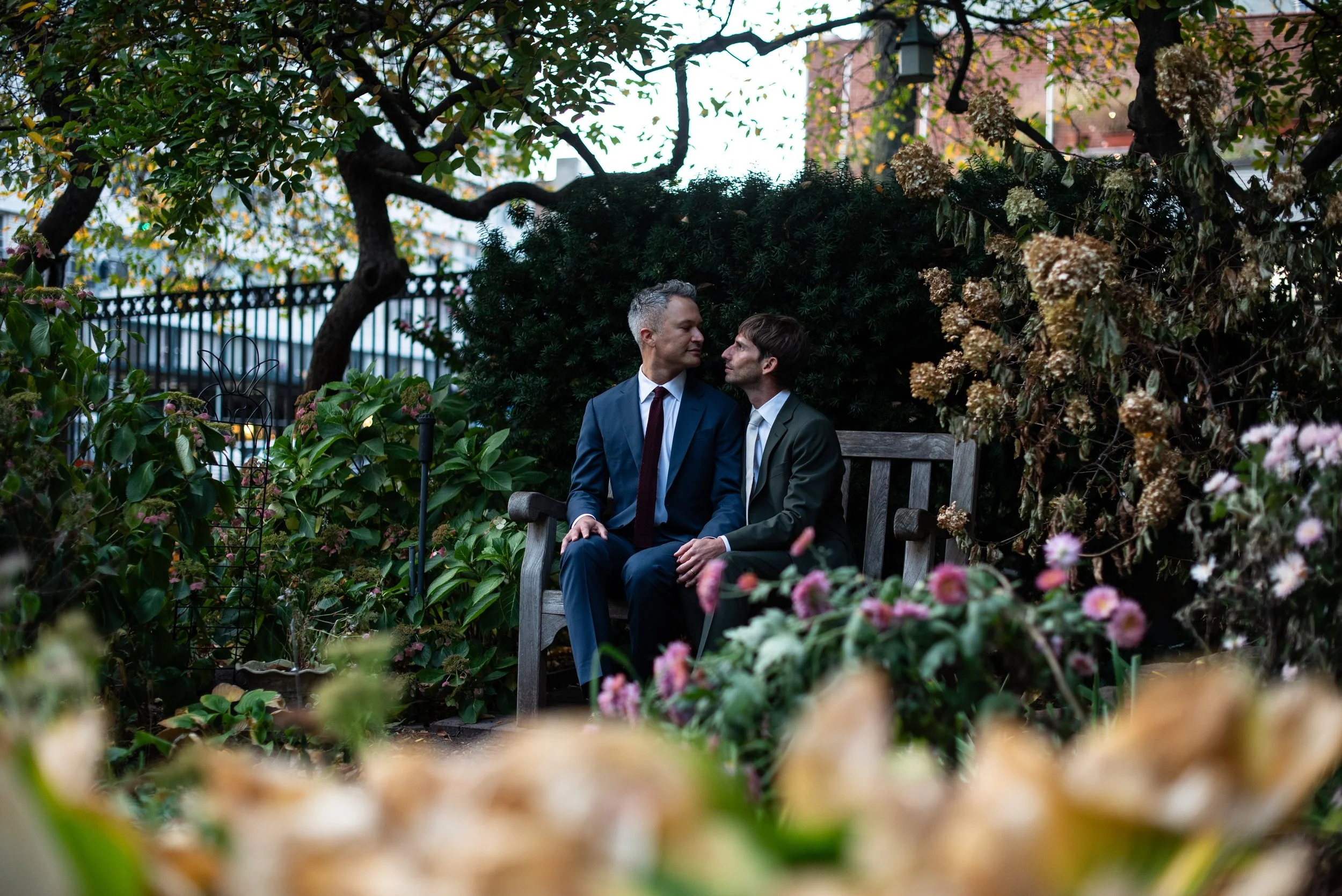 Two men sitting on a bench in Washington Square Park surrounded by foliage before their Cakewalk elopement ceremony.