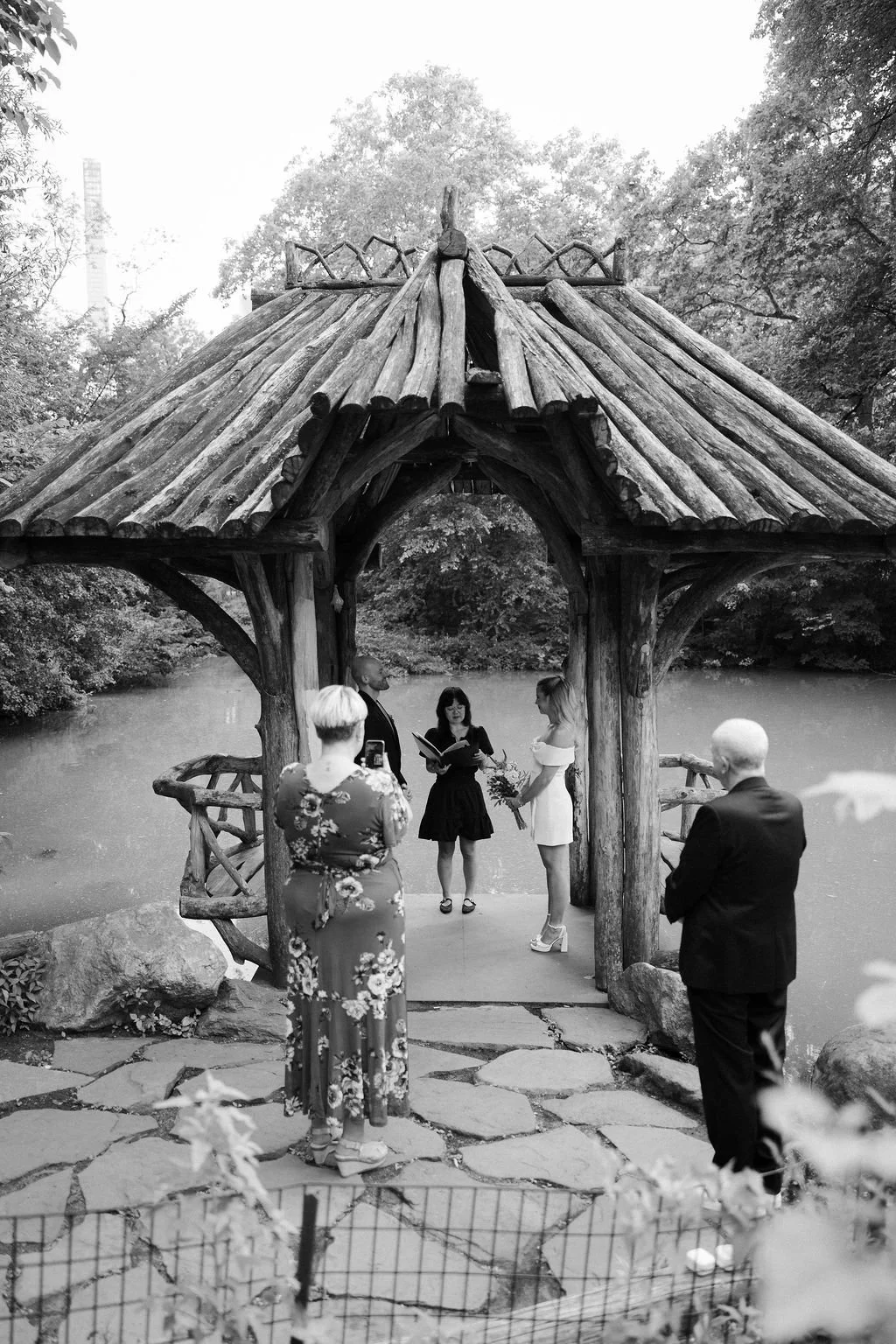 Wagner Cove wedding ceremony at Central Park, with bride and groom being married by officiant under the wooden lakeside pavilion during their Cakewalk NYC elopement.
