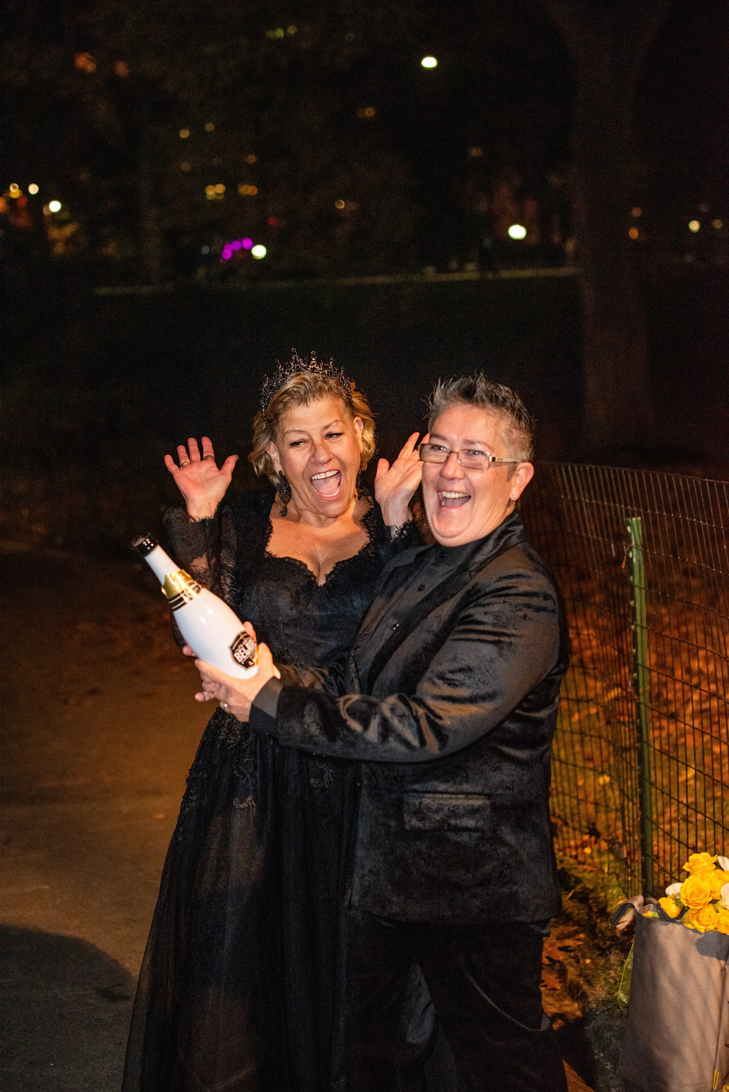 Two brides cheering and holding a bottle of champagne after their LGBTQ-friendly Cakewalk elopement.