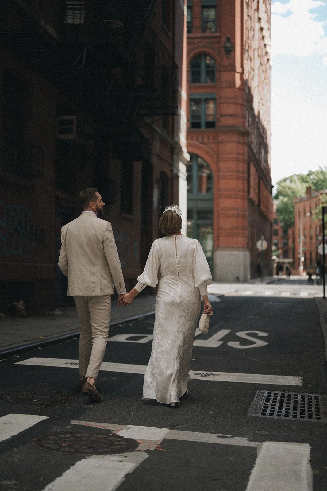 Bride and groom walking through SoHo streets staring up a tall brick buildings after their Cakewalk elopement. Includes crosswalk and street painting.