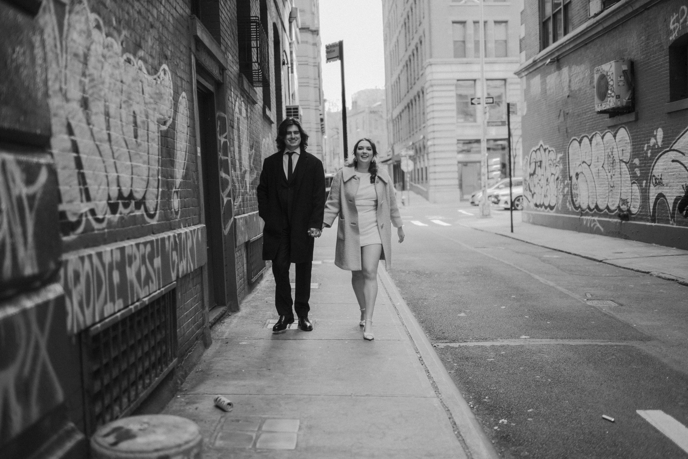 Black and white photograph of a couple walking together on a quiet New York City street after eloping.