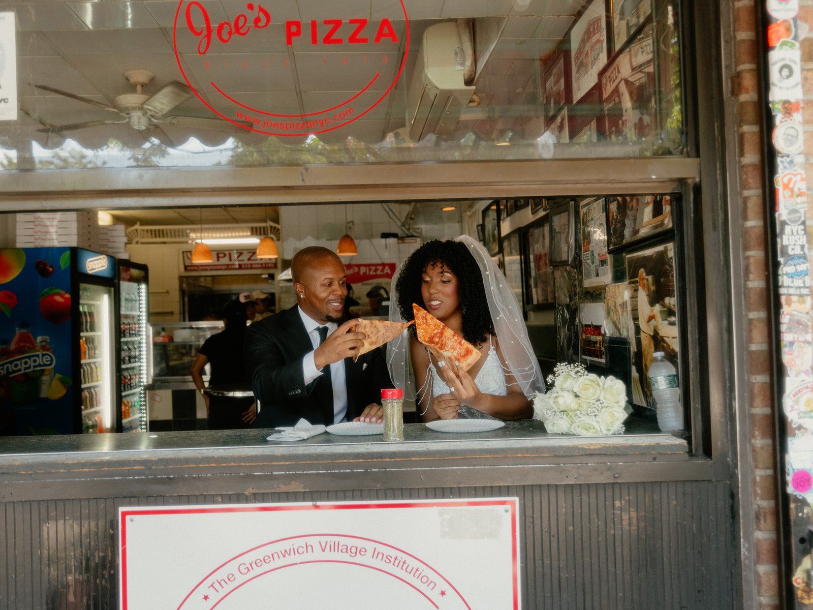 Bride and groom sharing slices of pizza at Joe's Pizza in NYC after their Cakewalk wedding ceremony.