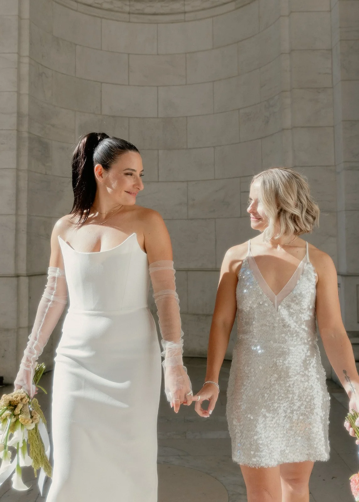 Two brides standing outside the New York Public Library looking at each other after their Cakewalk elopement.