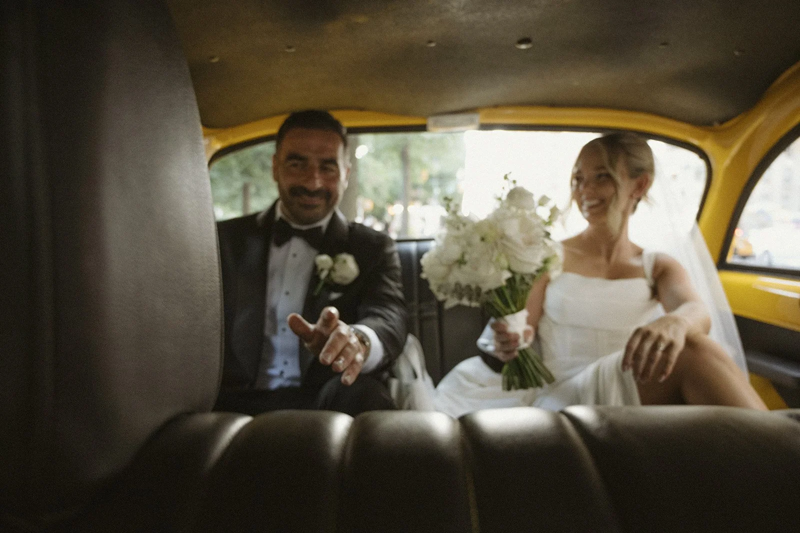 Bride and groom smiling inside the back seat of a vintage, yellow checkered NYC taxi after their Cakewalk wedding ceremony.