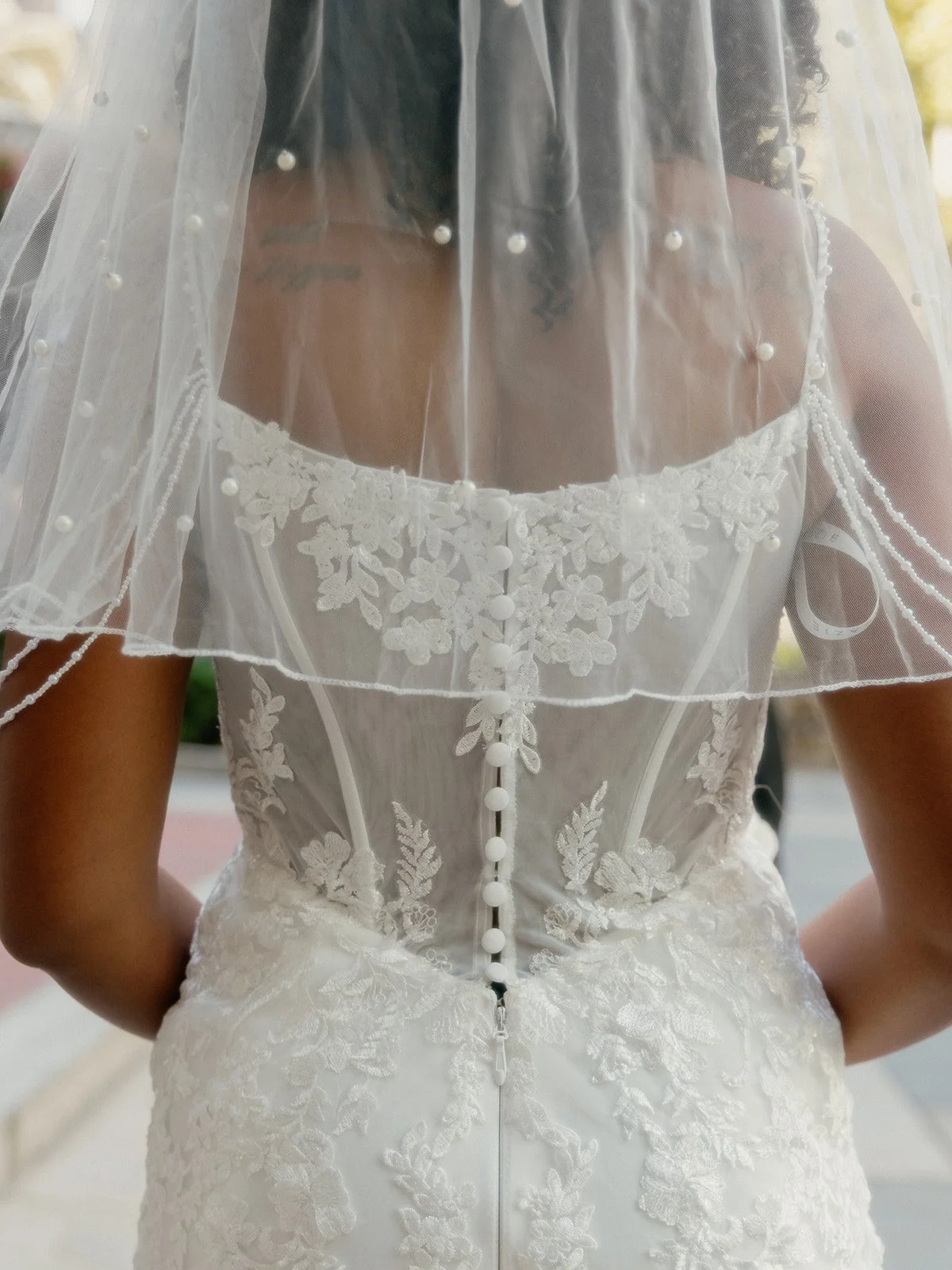 Details of the back of a bride's lace dress with a veil hanging down.