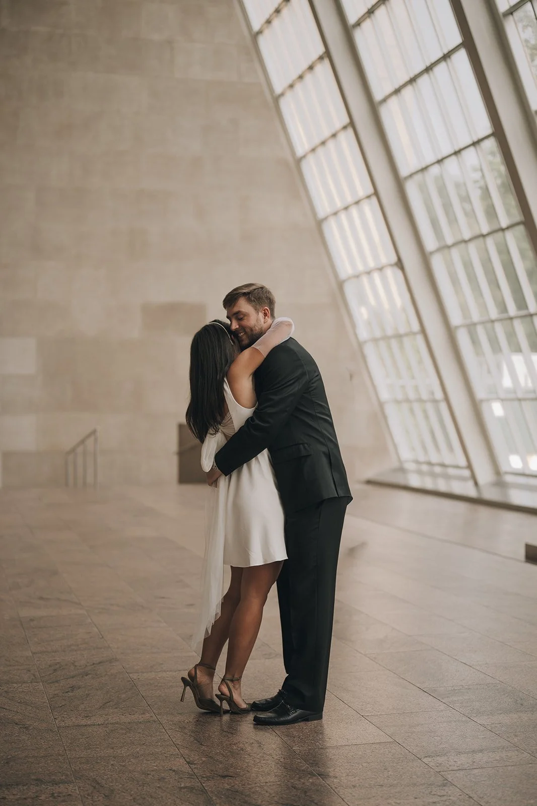 Bride and groom embracing inside the Met Museum of Art inside a beautiful glass wall surrounded by granite.