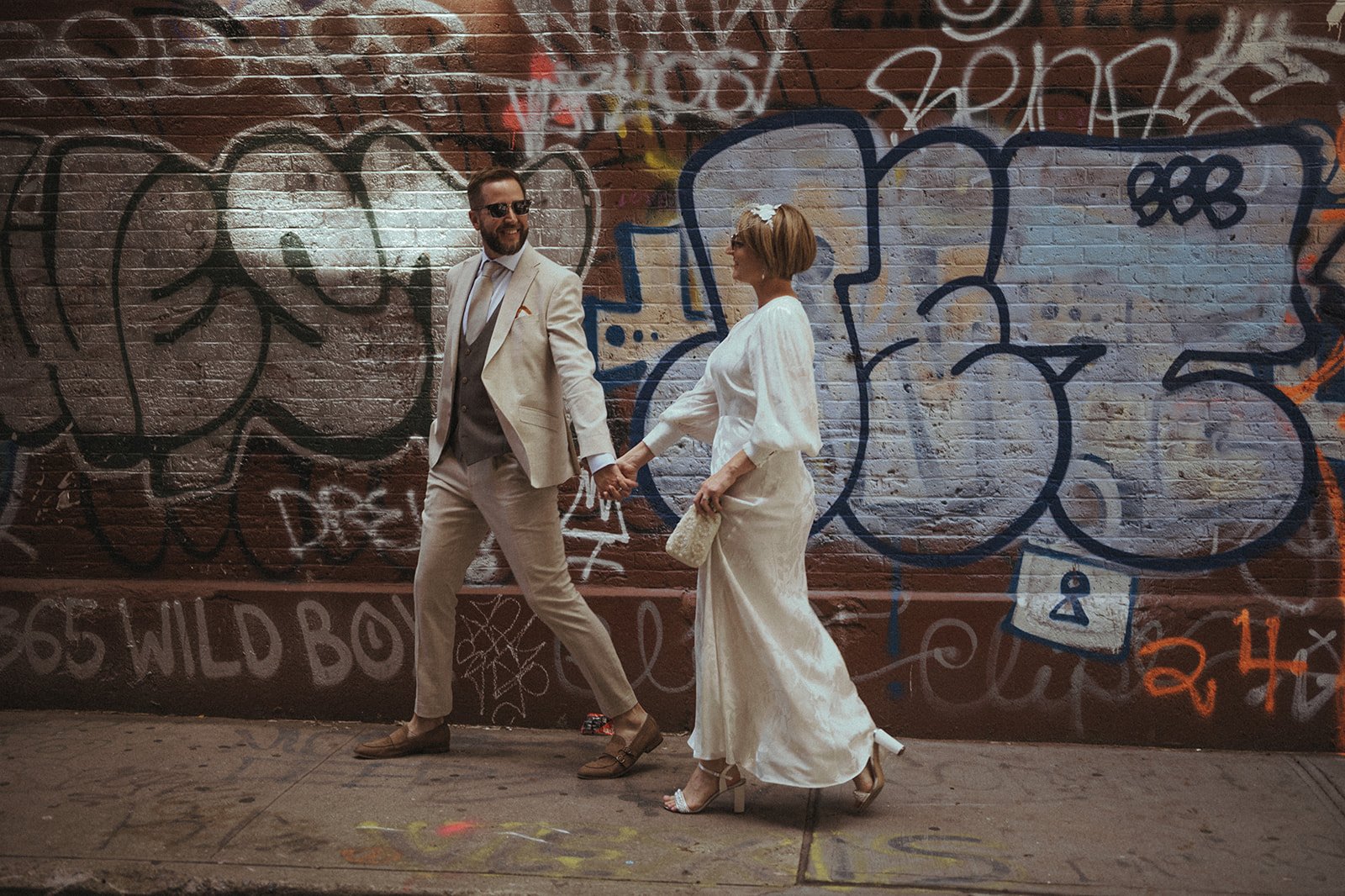 Bride and groom walk down a street with graffiti-covered walls in New York City.