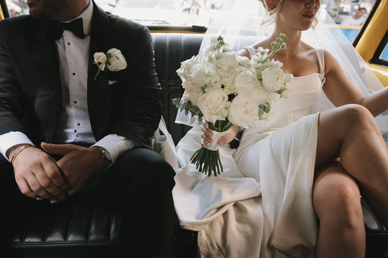 Close up of bride and groom seat in the back seat of a vintage yellow taxi holding a white bouquet.